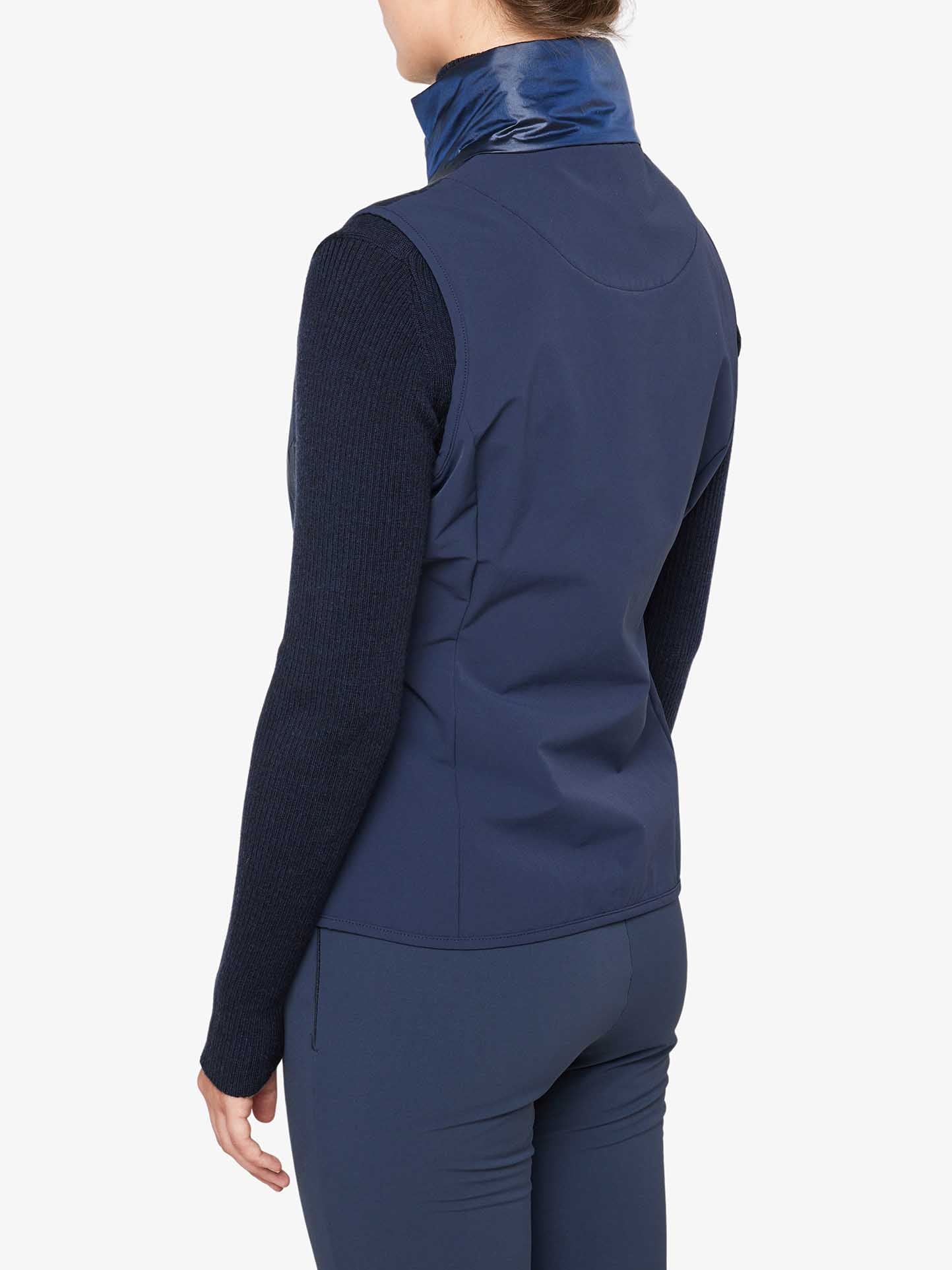 A person is seen from behind wearing a navy blue We Norwegians Beito Vest Women over a long-sleeve dark sweater and matching navy blue pants. The high collar of the wool padded vest is slightly turned up, and the background is plain white.