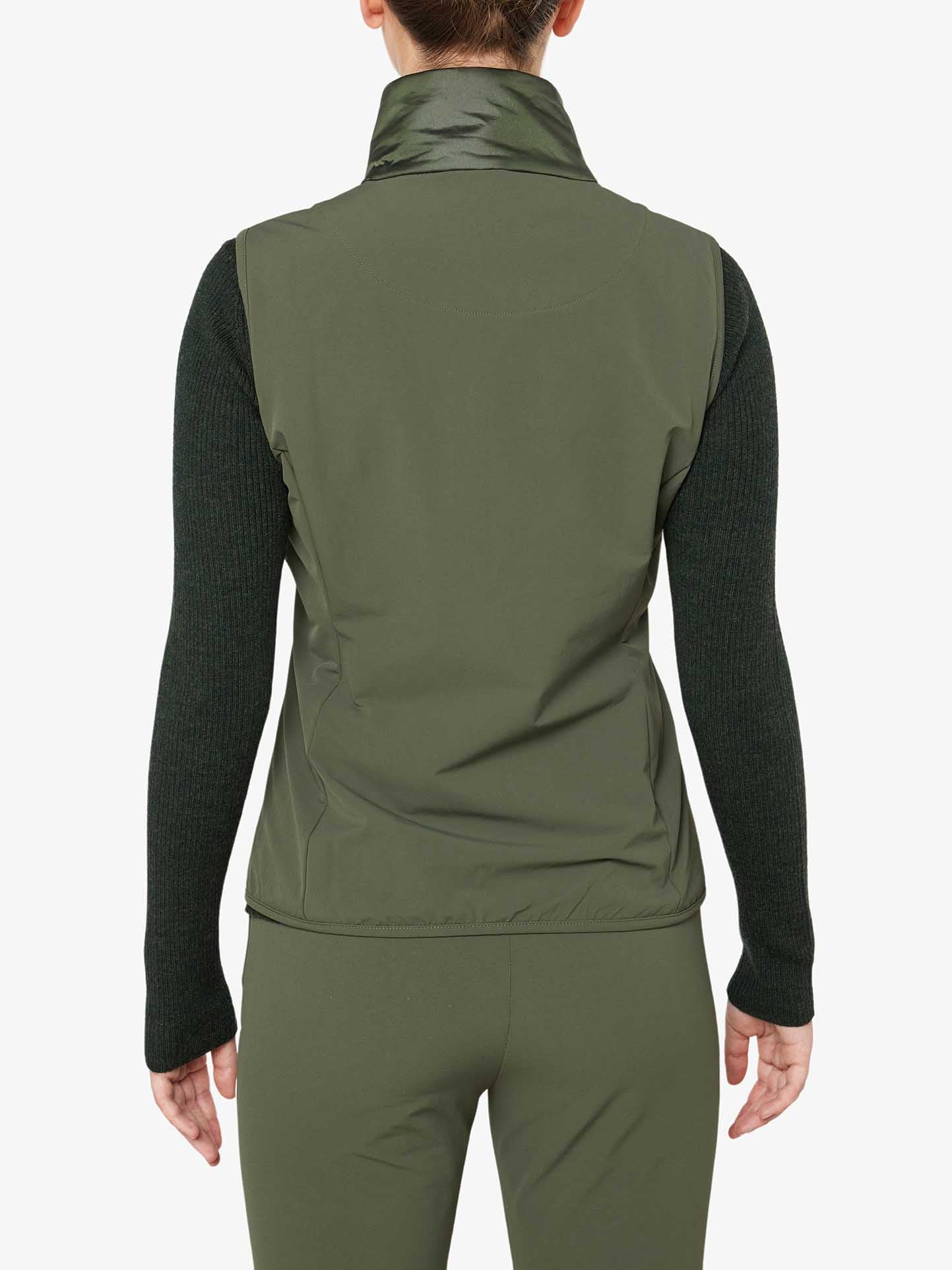 A person is shown from the back, wearing the olive green Beito Vest Women by We Norwegians over a dark long-sleeve top and matching green pants. The plain white background highlights the stylish outfit, while their hair is tied up, ready for cross-country skiing with both warmth and flair.