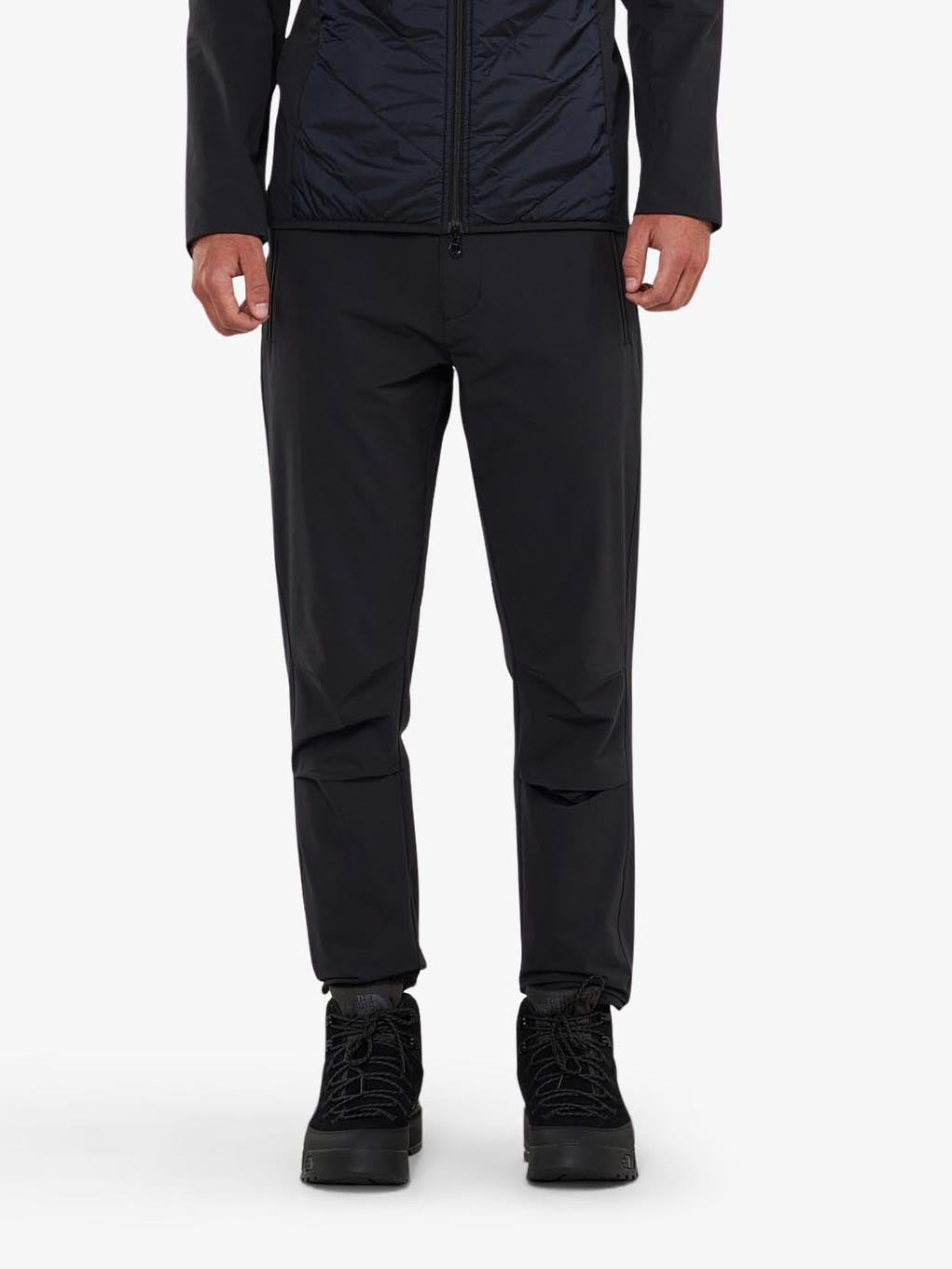 The individual wears Beito Pant Men by We Norwegians, crafted from breathable fabric ideal for outdoor adventures. Against a plain white background, their relaxed stance in black boots highlights the apparel from neck to toe.