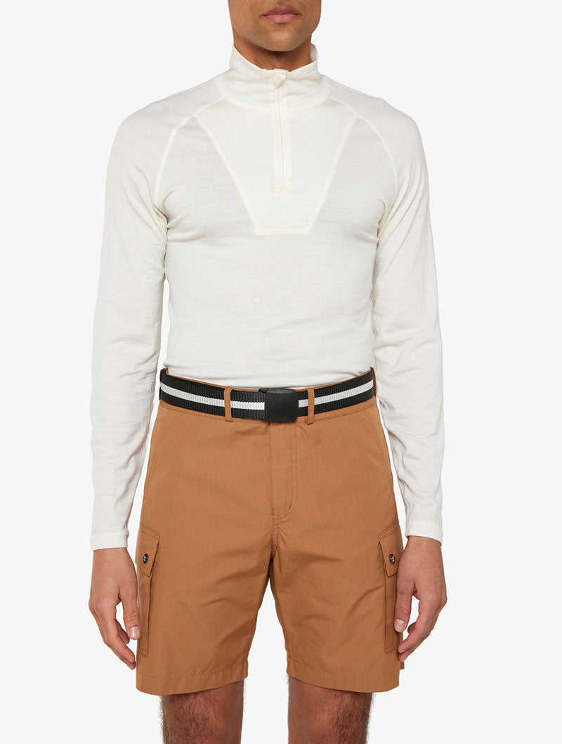 A person is wearing a white long-sleeve, zip-up top paired with light brown cargo shorts. They also have the Vidda Belt from We Norwegians, which is adjustable and features black and white stripes. The background is plain white.