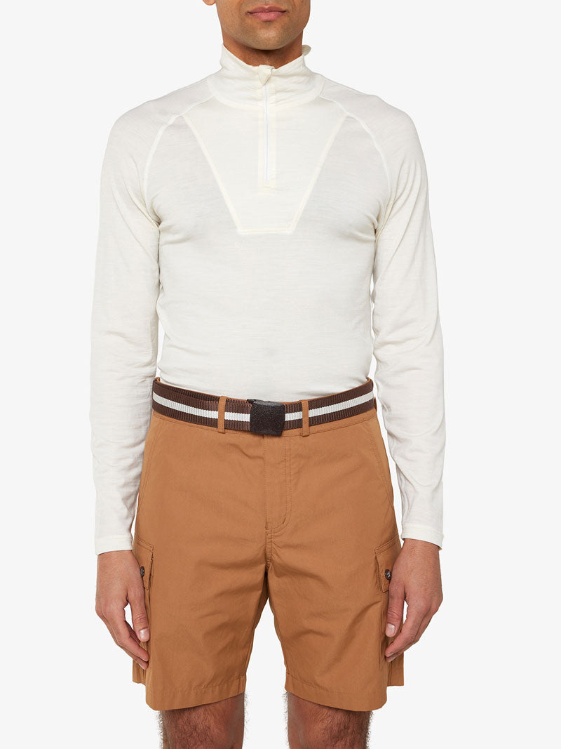 A person is wearing a white long-sleeve shirt with a quarter-zip neckline and light brown cargo shorts. The individual has an adjustable black Vidda Belt by We Norwegians, a versatile unisex accessory, with a rectangular buckle fastened around their waist. The background is plain white.