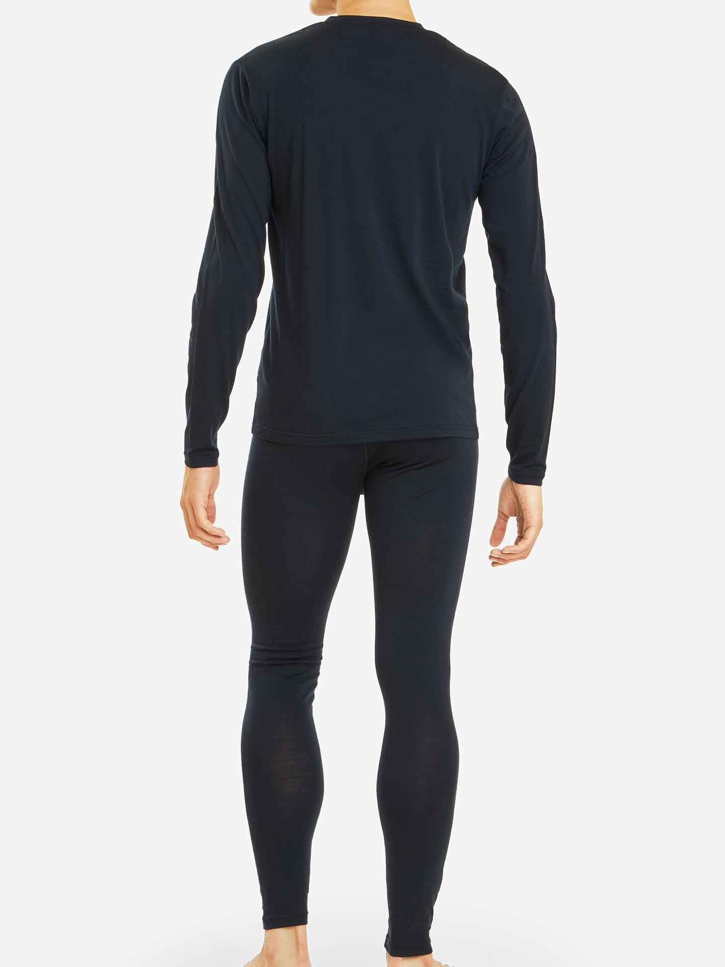 A person stands barefoot, facing away in a Sno Merino Long Sleeve Men top and matching leggings by We Norwegians. The outfit is crafted from breathable fabric on a plain white background.