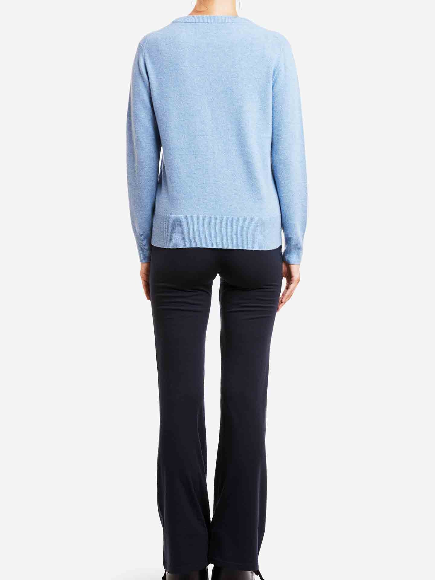 A person is shown from the back, wearing a light blue Blefjell Cashmere Crewneck Women by We Norwegians and black pants. The background is plain white, highlighting this luxury staple without any distractions. The person's head is not visible in the image.