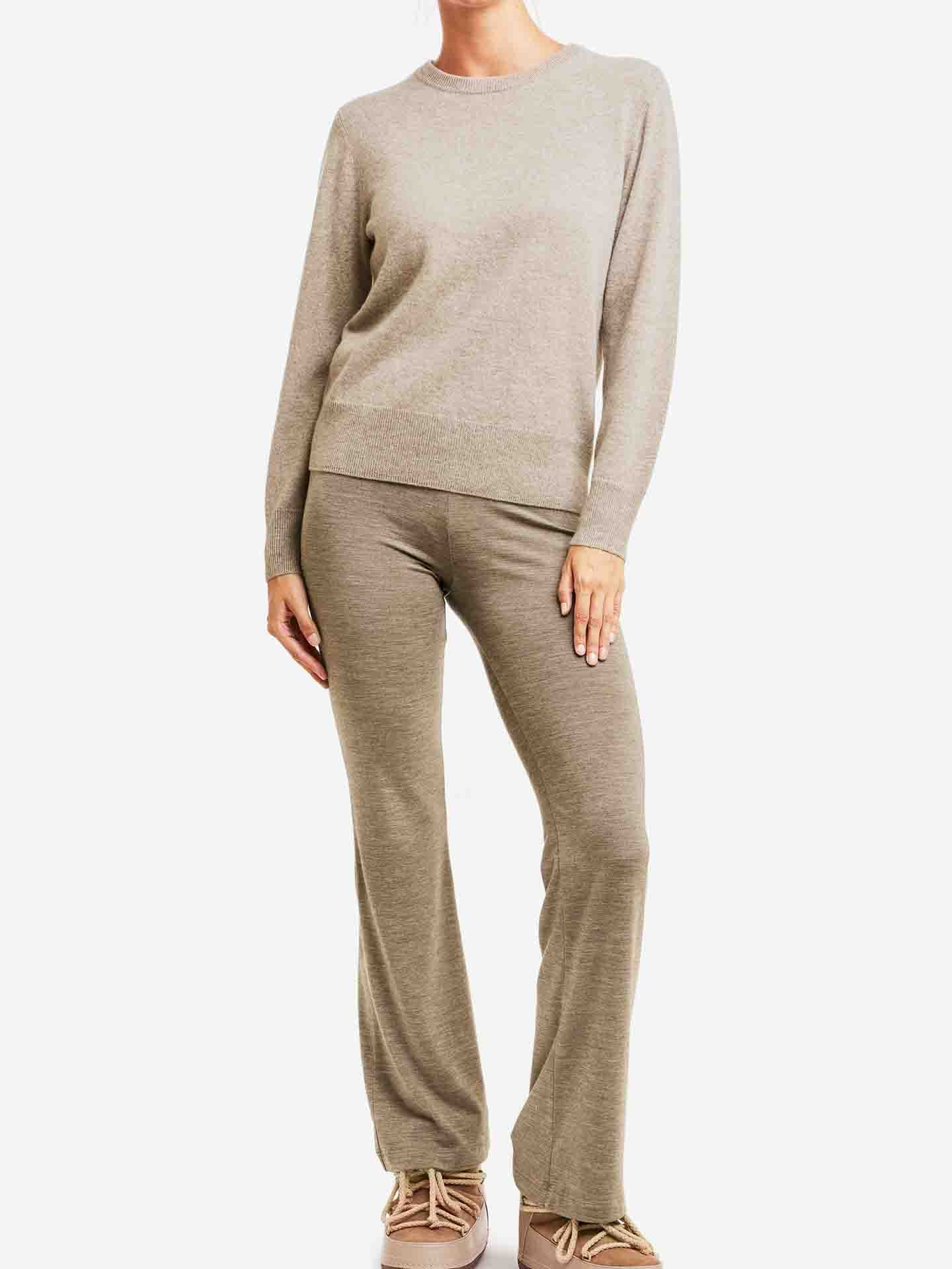 A woman is wearing a light beige, pure cashmere Blefjell Cashmere Crewneck Women sweater by We Norwegians, paired with matching pants and shoes. Her face is not visible as she stands with a relaxed posture against a plain white background, perfectly complementing this luxury staple.