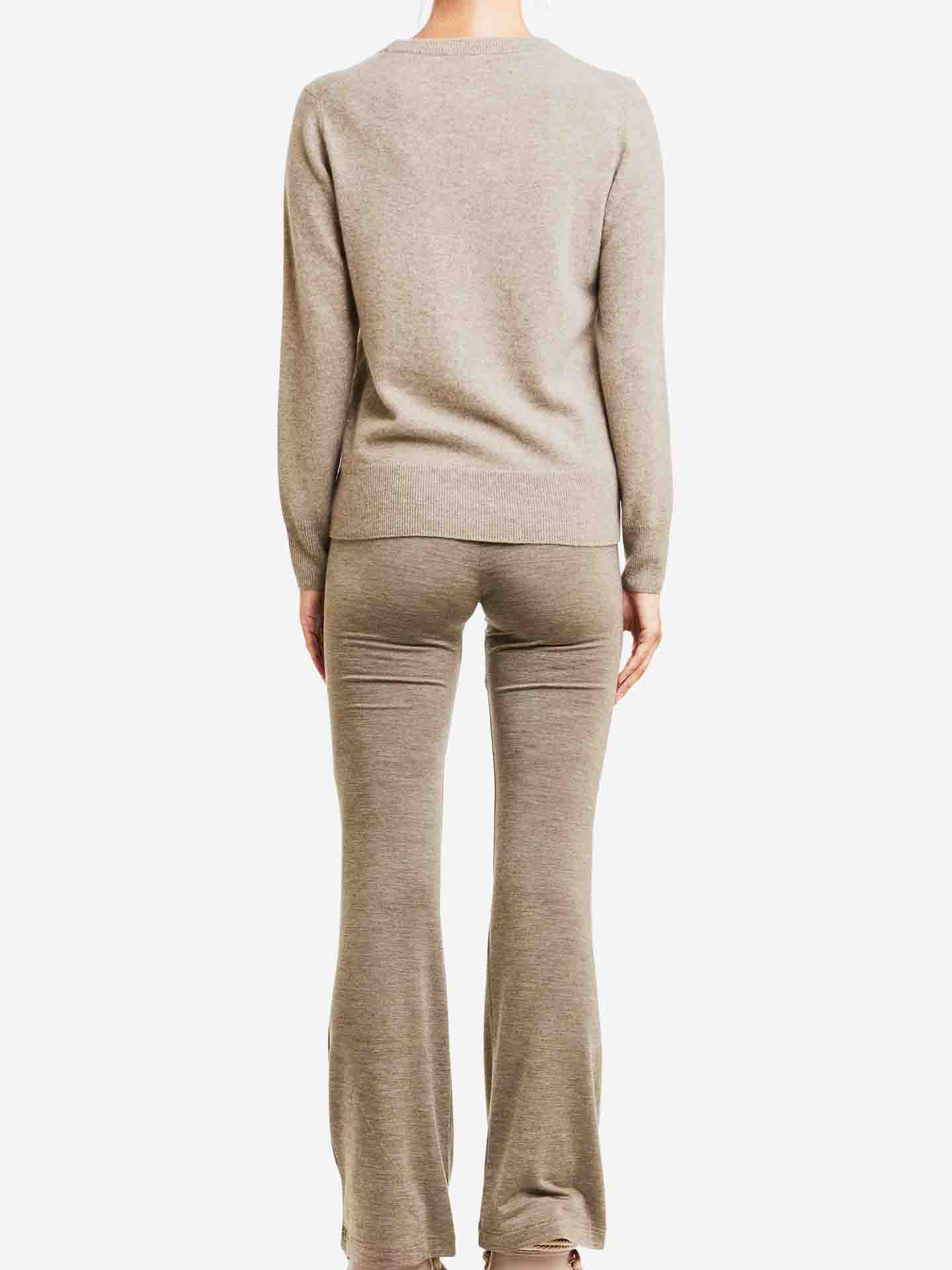 Person wearing a beige knit sweater and flared knit pants, facing away from the camera against a plain white background. The ensemble features the luxurious Blefjell Cashmere Crewneck Women by We Norwegians, making it a true luxury staple.