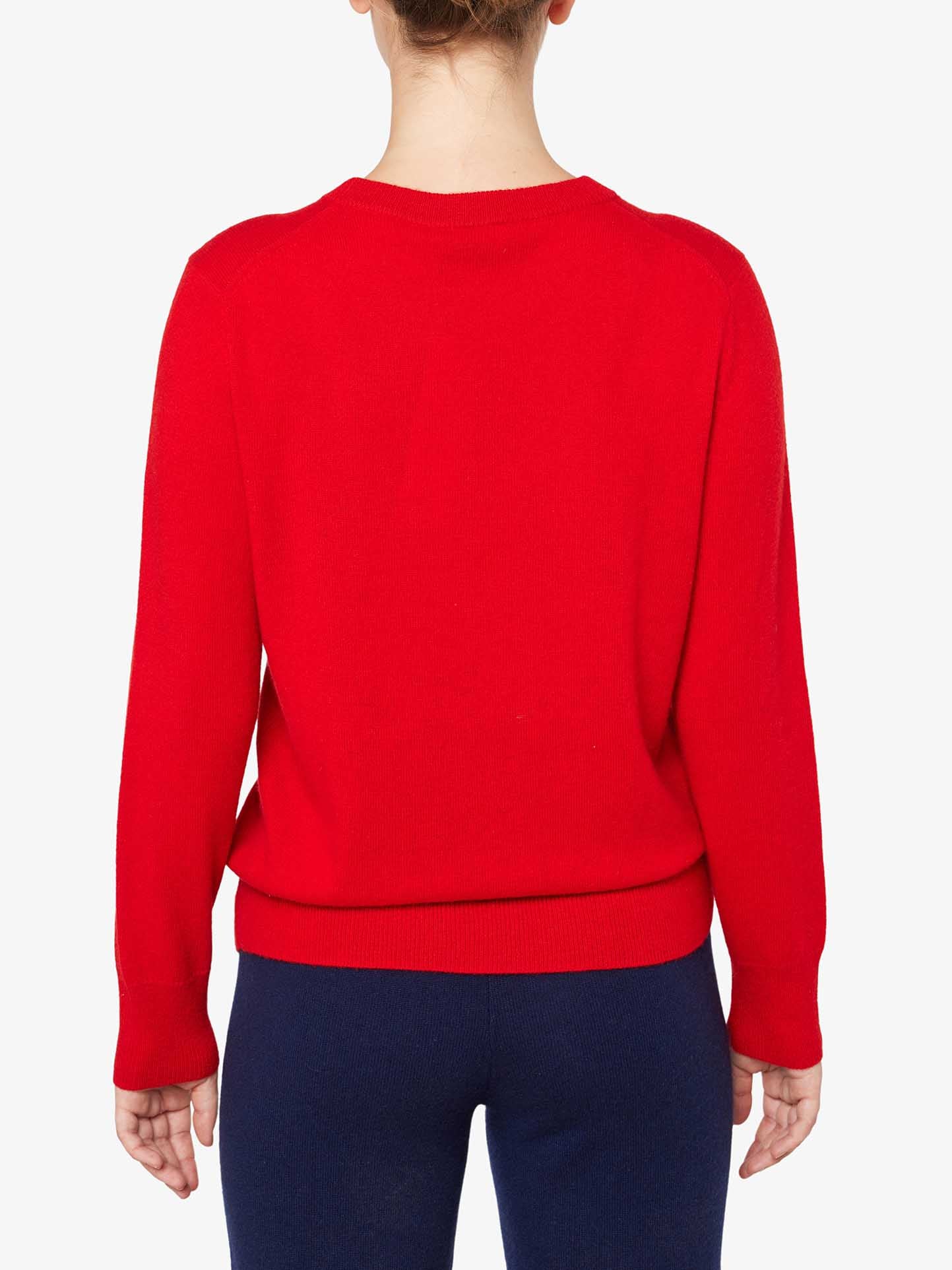 A person, seen from behind, is wearing the Blefjell Cashmere Crewneck for Women by We Norwegians in a vibrant red with navy blue bottoms against a plain white background. This luxurious pure cashmere top features a simple round neckline and a relaxed fit. The person's hair is tied up, and their hands are resting by their sides.