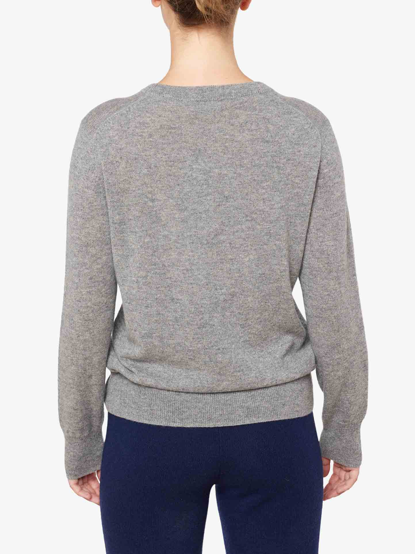 Rear view of a person wearing a gray We Norwegians Blefjell Cashmere Crewneck Women and dark blue pants. The individual's head is turned slightly to the right. The pure cashmere sweater boasts a simple, classic design with no visible patterns or embellishments, making it a true luxury staple.