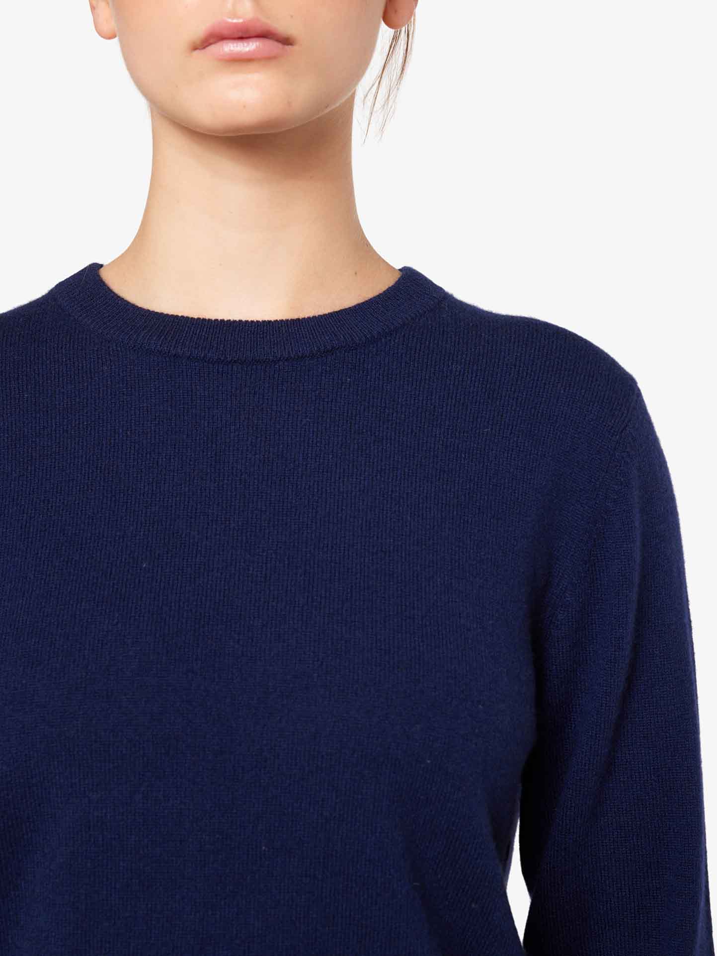 A person is shown from the upper torso up, wearing a luxurious navy blue sweater. Their face is partially visible, focusing on the lower half, with their lips closed. The plain white background highlights the elegance of this Blefjell Cashmere Crewneck Women by We Norwegians, made of pure cashmere.