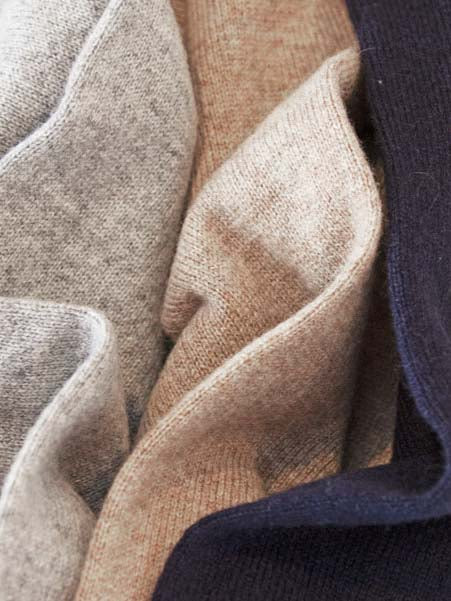 Close-up of a cozy knit fabric in overlapping folds. The warm texture, crafted from pure cashmere yarn, showcases colors of light gray, beige, and dark blue—inviting both comfort and luxury with the Blefjell Cashmere Crewneck Men by We Norwegians.