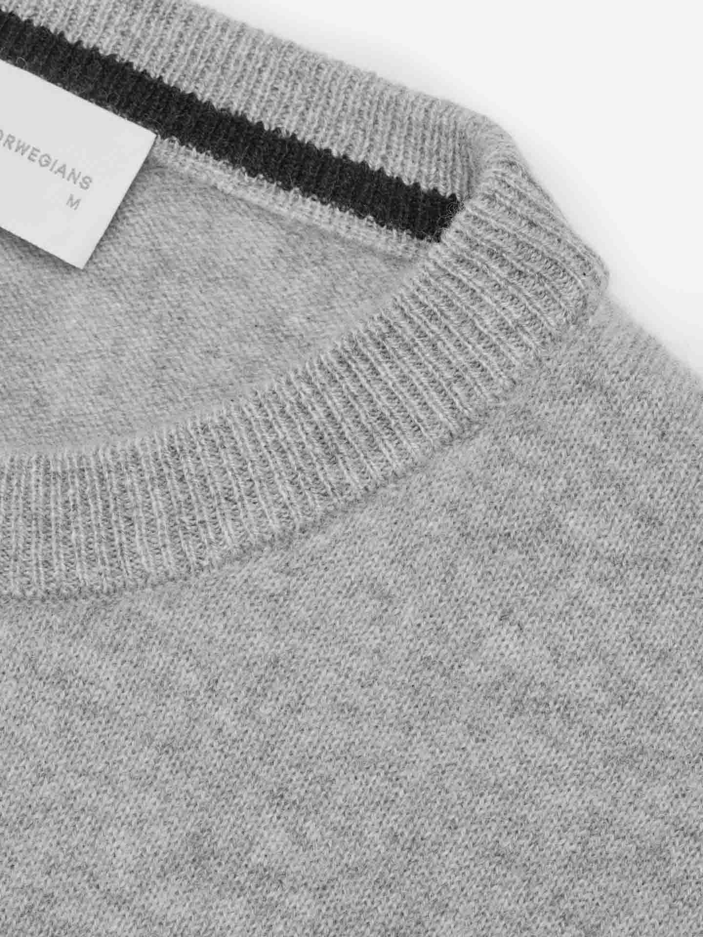 Close-up of the We Norwegians Blefjell Cashmere Crewneck Men sweater with a ribbed collar. The collar features a black stripe near the top. A white tag with text is partially visible, indicating the size "M" at the top left of the image. The fabric, crafted from pure cashmere yarn, appears soft and slightly textured.