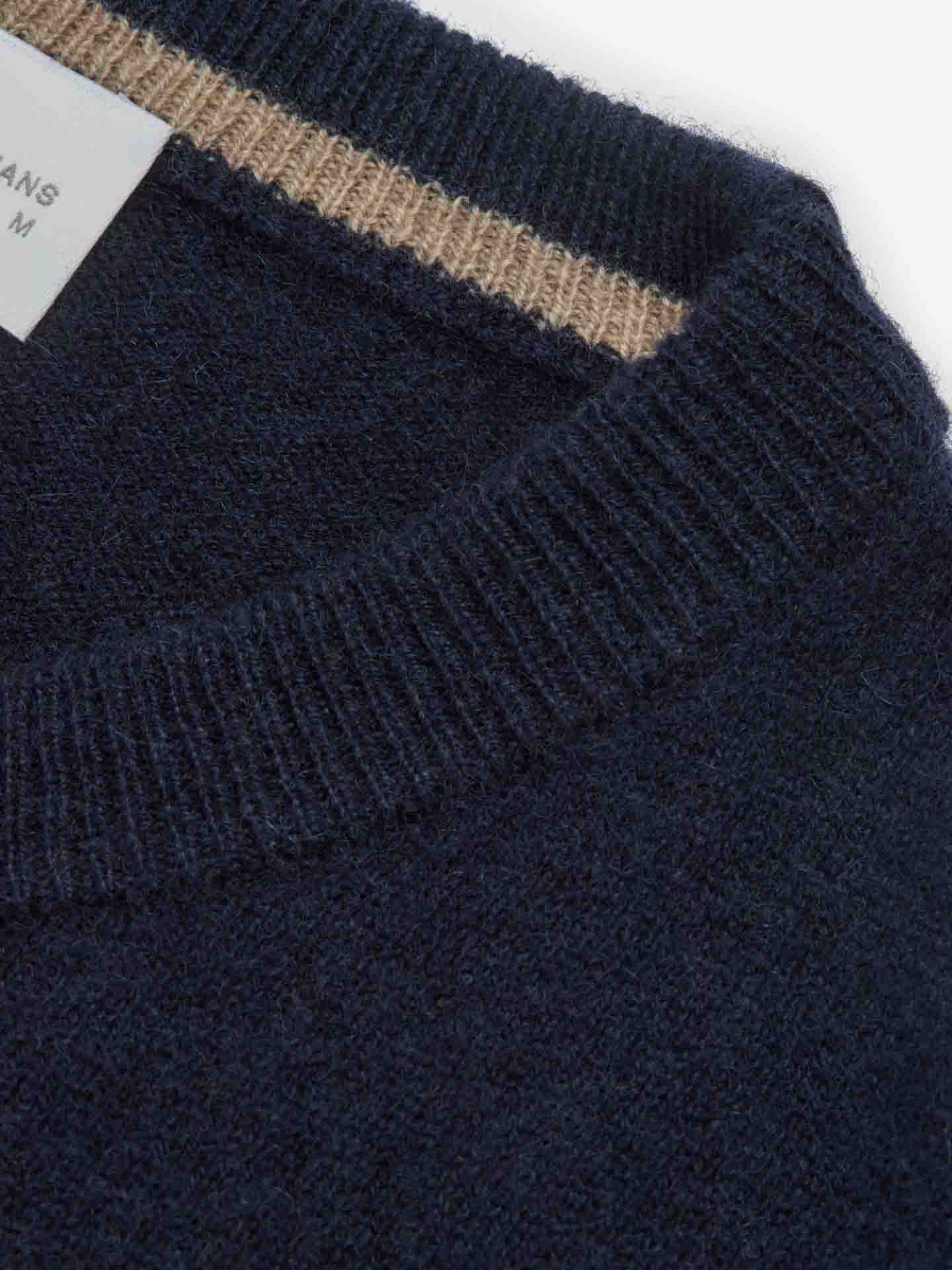 Close-up of a dark blue knitted collar with a ribbed texture and a subtle beige stripe along the inner edge. Tucked inside the collar is a portion of a white clothing label with text, hinting at the luxurious Blefjell Cashmere Crewneck Men sweater from We Norwegians, crafted from pure cashmere yarn.