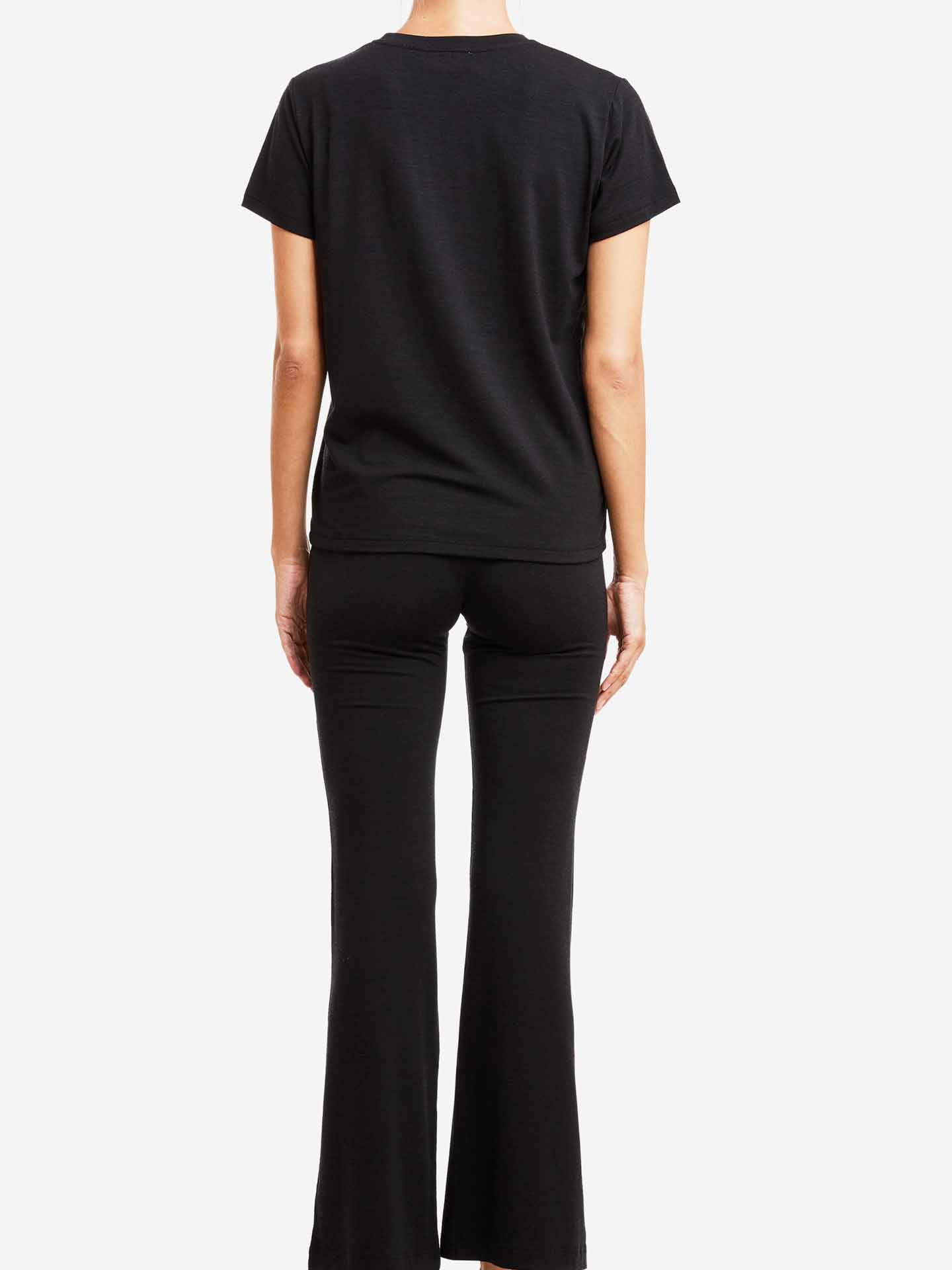 Revised Sentence: Rear view of a person wearing the Hygge Tee Women by We Norwegians and black flared pants, standing against a white background. The simplicity of their outfit is elevated by the comfort reminiscent of merino wool, offering a touch of luxury base layer sophistication.