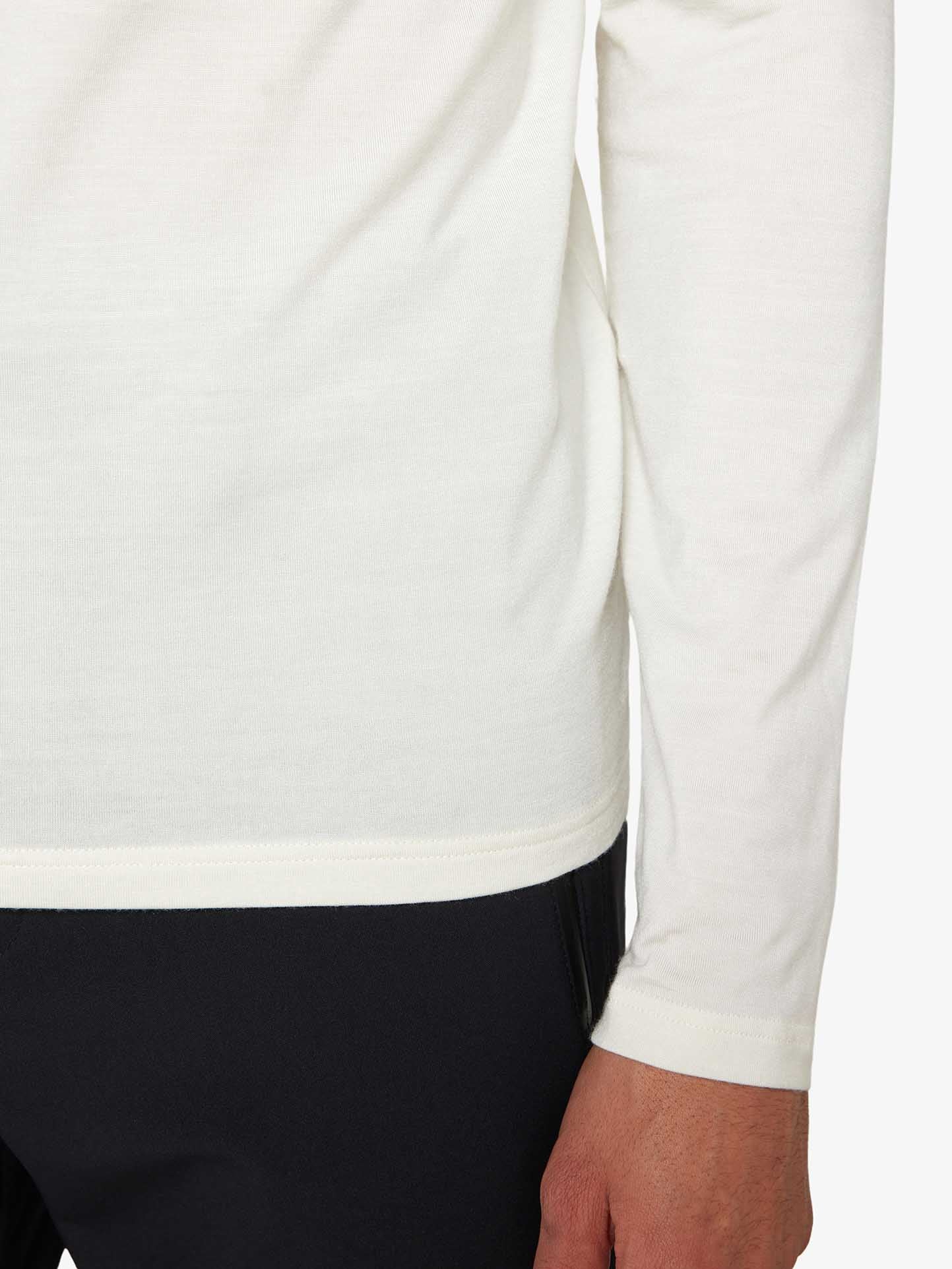 Close-up view of a person wearing the versatile Hygge ZipUp Men by We Norwegians: a long-sleeved white shirt paired with black pants. The focus is on the lower part of the torso, showcasing the right hand hanging by the side and part of the arm. The background is plain and unobtrusive.