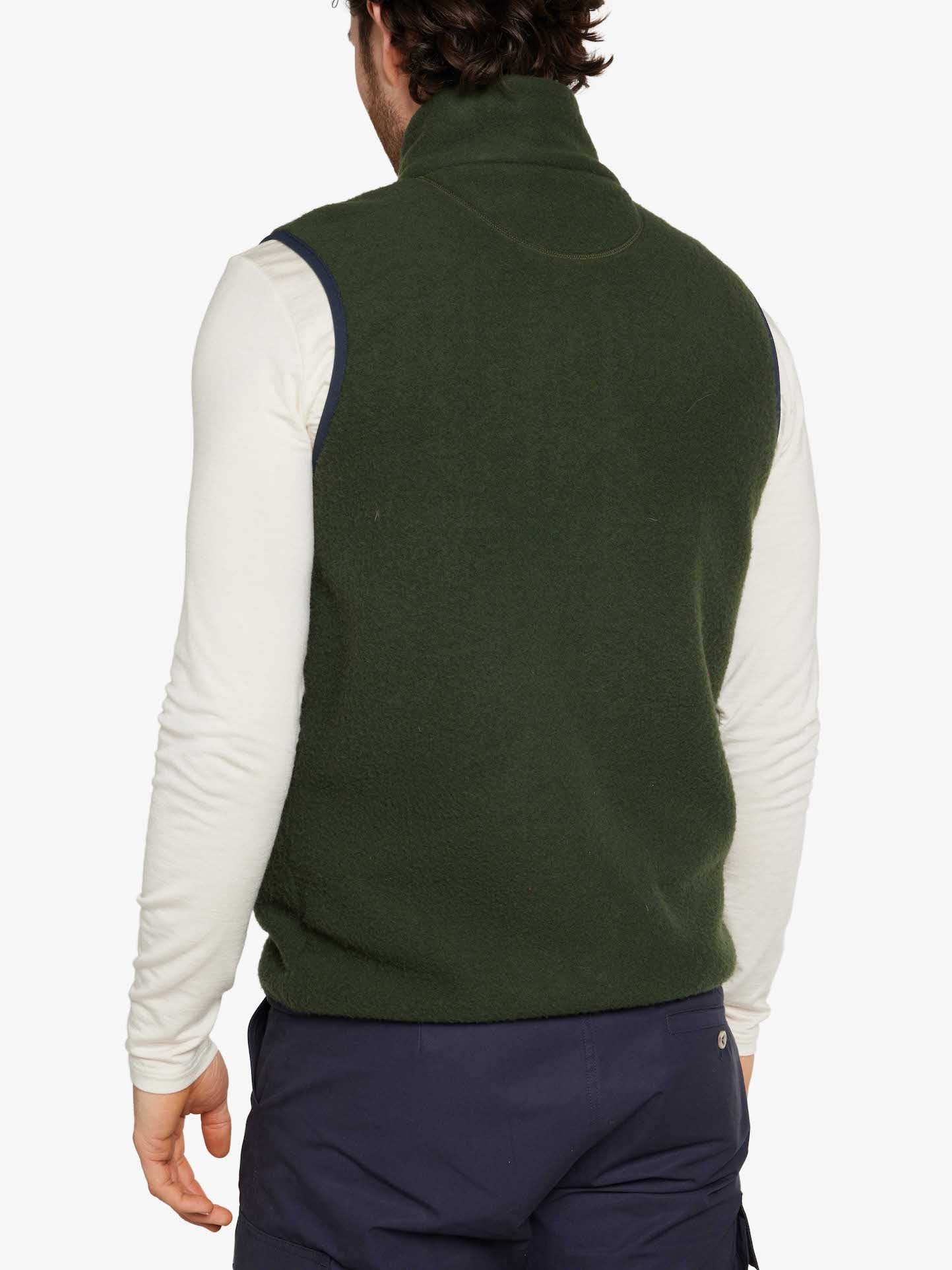 A person with dark hair, seen from behind, is wearing a Svalbard Vest Men by We Norwegians. The sleeveless green Merino fleece vest is layered over a long-sleeved white shirt. The individual is also sporting regular fit dark blue pants against a plain white backdrop.