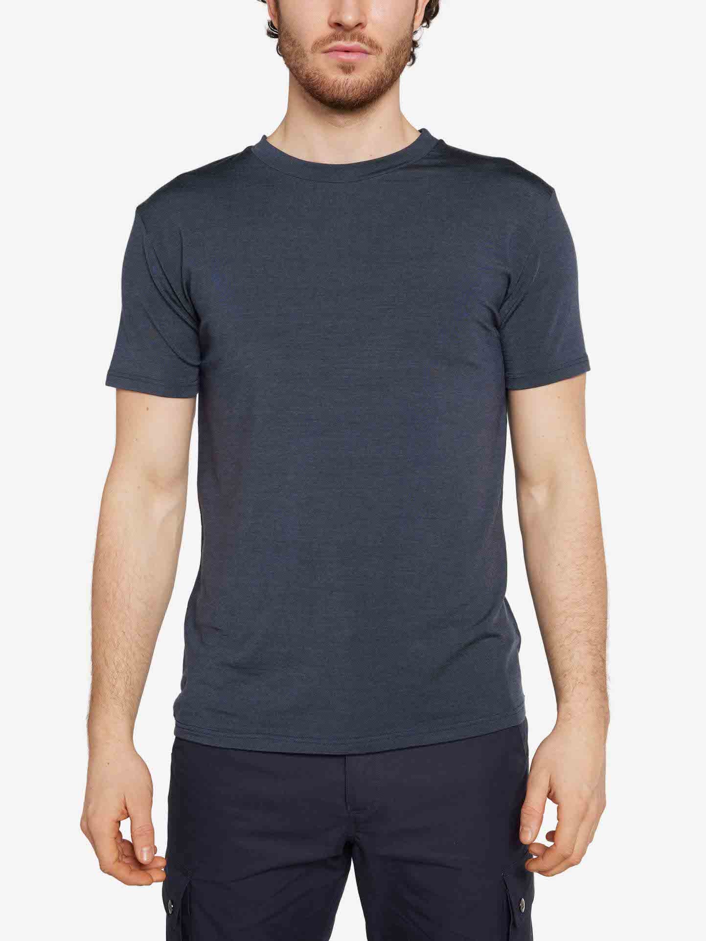 A man with short dark hair and a beard is wearing the Hygge Tee Men by We Norwegians, a plain dark blue fitted Merino wool t-shirt with a crew neckline and short sleeves, paired with dark pants. He is standing against a white background with his arms relaxed at his sides.