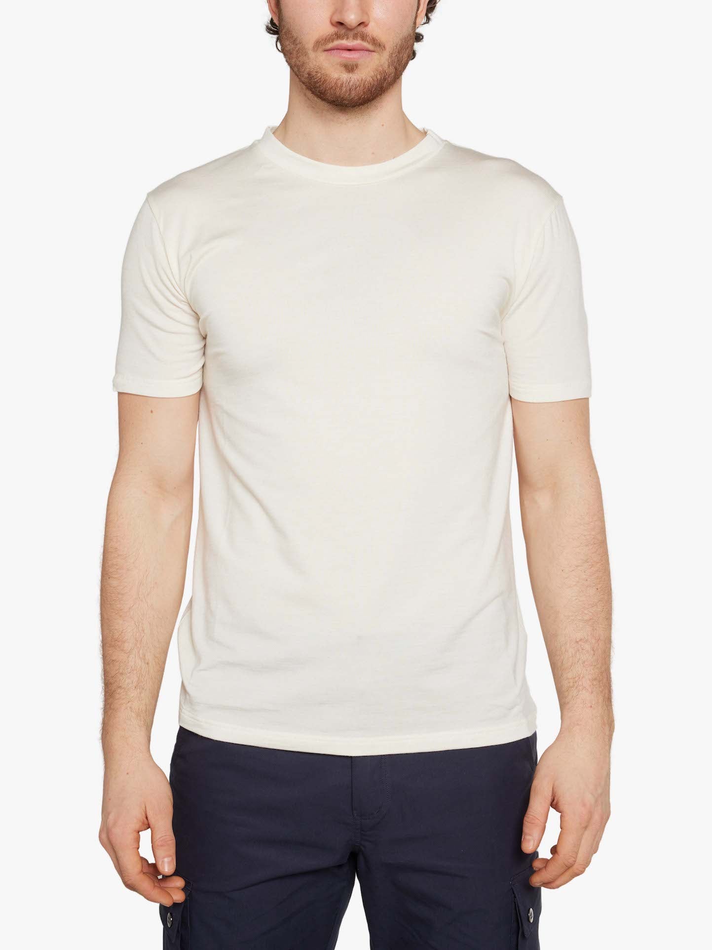 A person with short hair is wearing a plain, short-sleeved, white Hygge Tee Men by We Norwegians and dark pants. They are standing against a white background, facing forward with their arms relaxed at their sides.