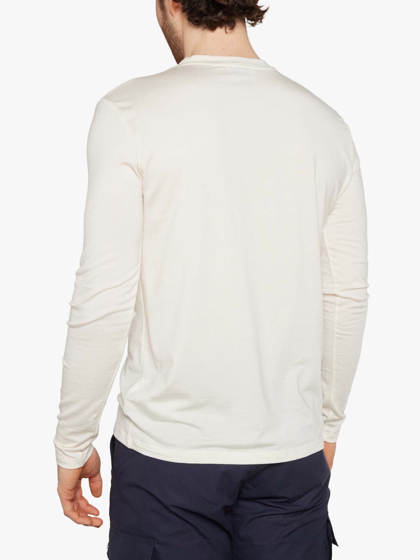 A person with short, dark hair is shown from the back, wearing the Hygge LongSleeve Men by We Norwegians, a light-colored shirt made of cozy Merino wool, paired with dark pants. The background is plain white.