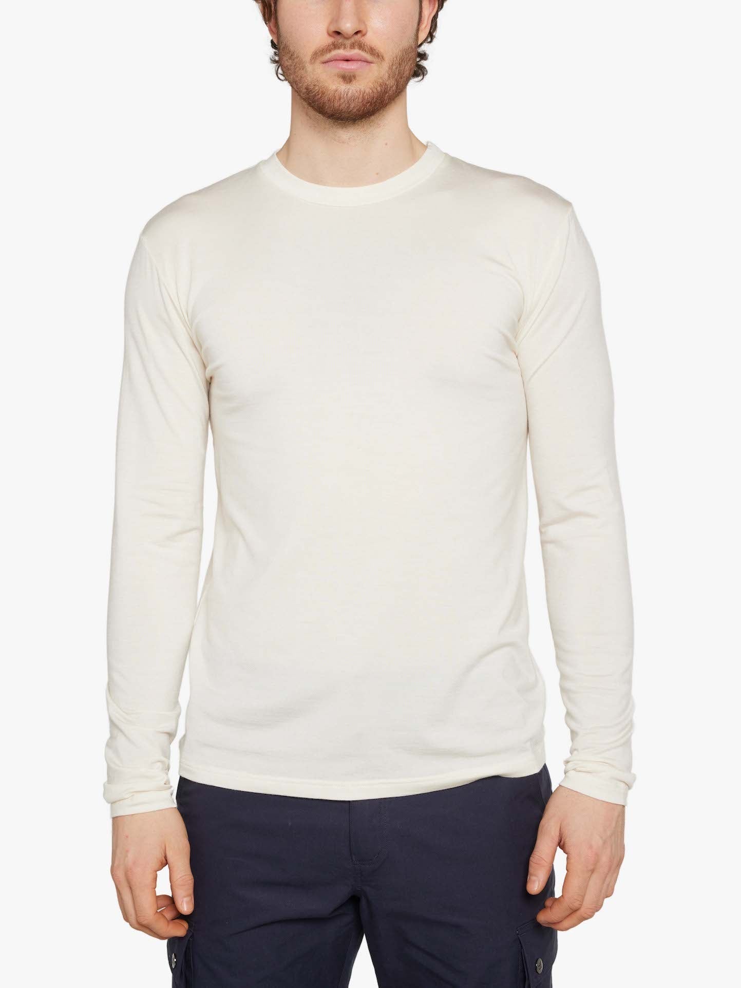 A man with short hair and partial facial hair is wearing a plain, long-sleeved Hygge LongSleeve Men shirt by We Norwegians in off-white and dark pants. He is standing facing the camera against a white background.