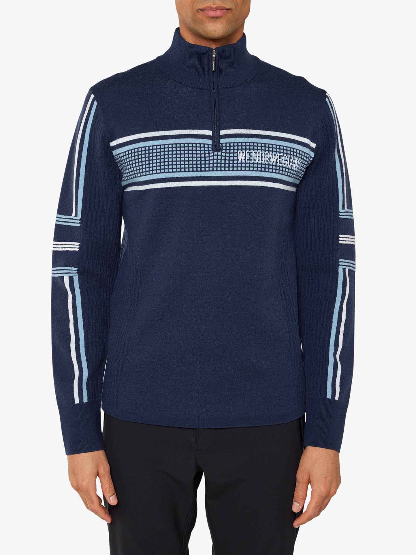 A man is wearing a navy blue Stryn Zipup Men sweater from We Norwegians, which features light blue and white stripes across the chest and down the arms. Made from ultrafine merino wool, the sweater has a ribbed pattern on the sides and sleeves. He is also wearing black pants against a plain white background.