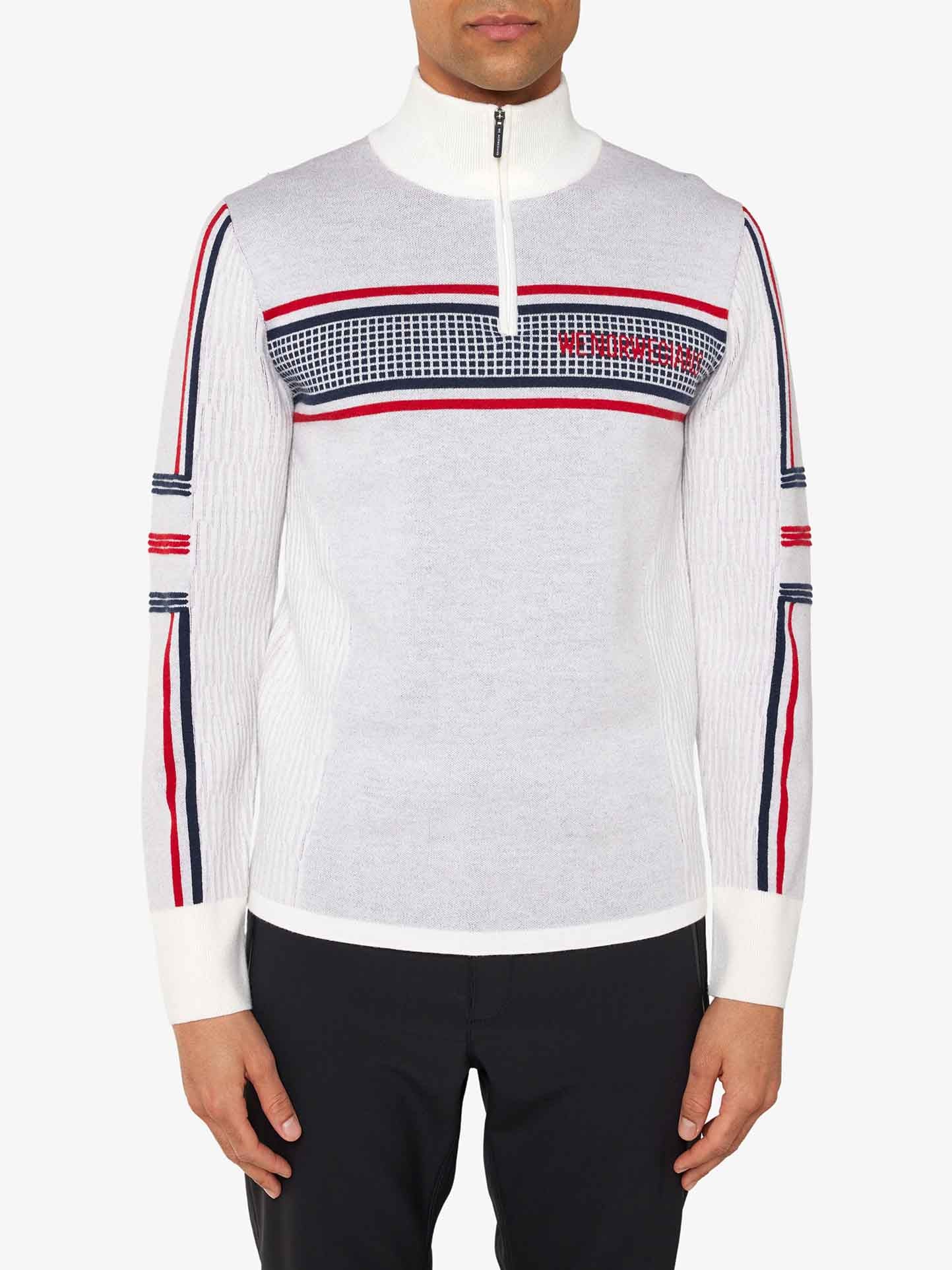 A person is wearing the Stryn Zipup Men by We Norwegians, a retro ski sweater made of ultrafine merino wool with white ribbed fabric featuring red, black, and blue stripes along the shoulders and sleeves. The half-zip collar and grid pattern across the chest displaying "PEUTEREY" in red complete the look. They are also wearing black pants.