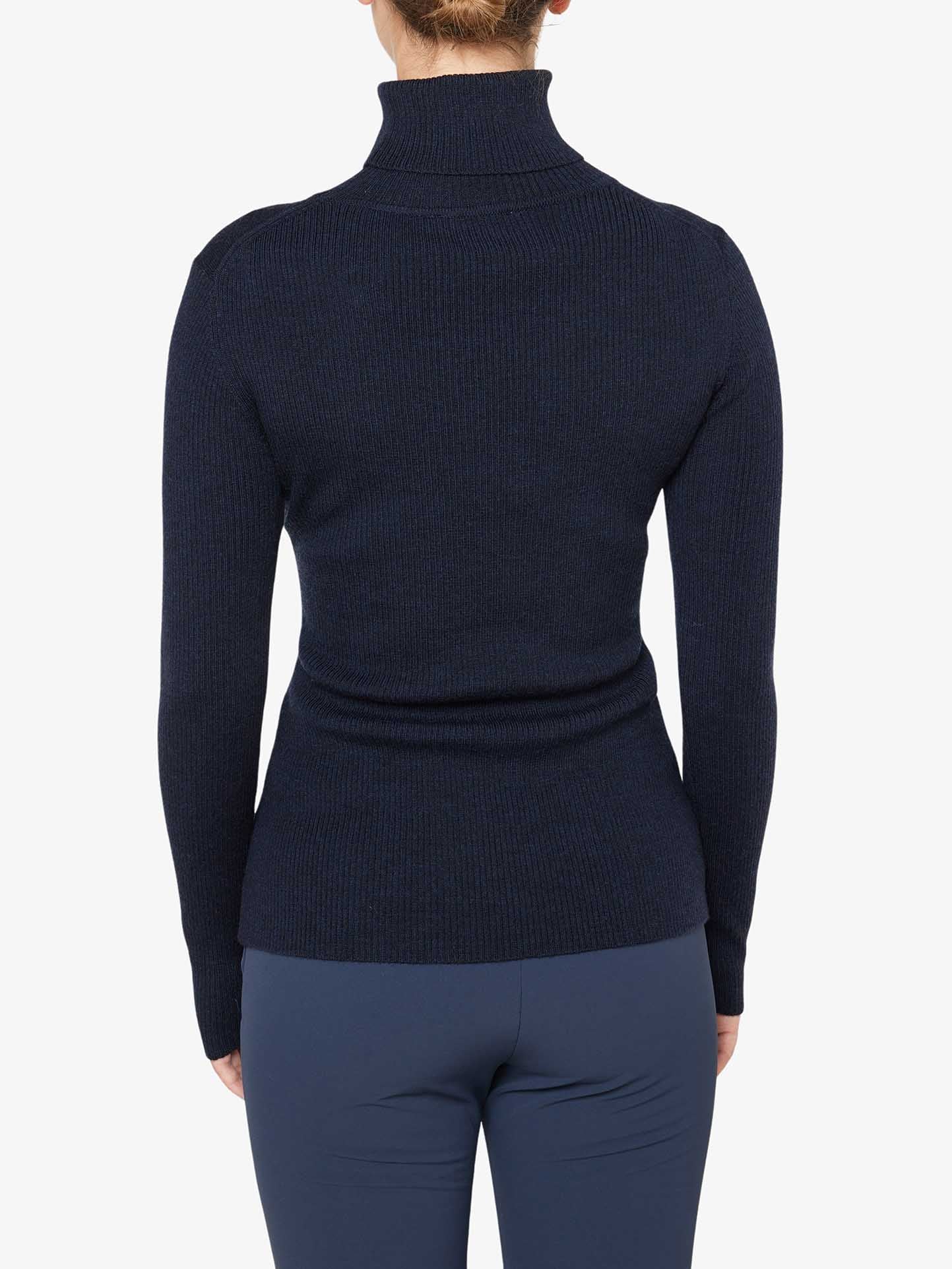 A person is standing with their back to the camera, wearing a fitted, long-sleeved, dark blue Signature Rollneck Women top by We Norwegians and dark pants. The background is a plain, light gray color.