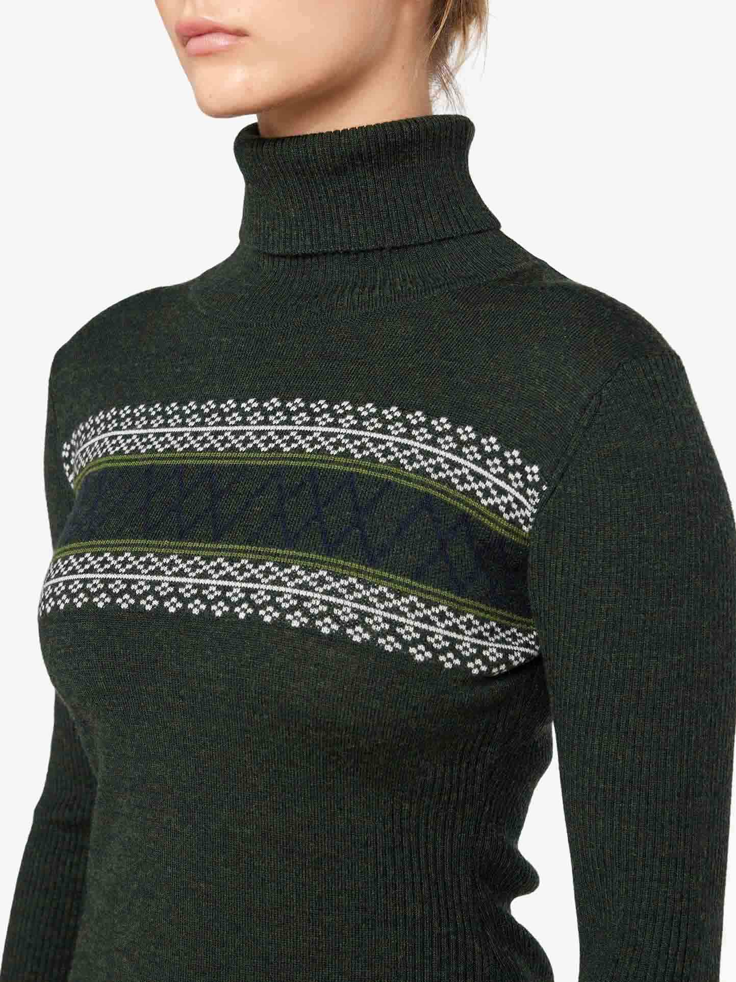 A person wearing the Signature Rollneck Women by We Norwegians, featuring a dark green color with a patterned horizontal stripe across the chest. The background is plain white. Crafted from fine Merino wool, this sweater boasts a textured knit and geometric design in contrasting white and olive tones. The person's face is partially out of the frame.