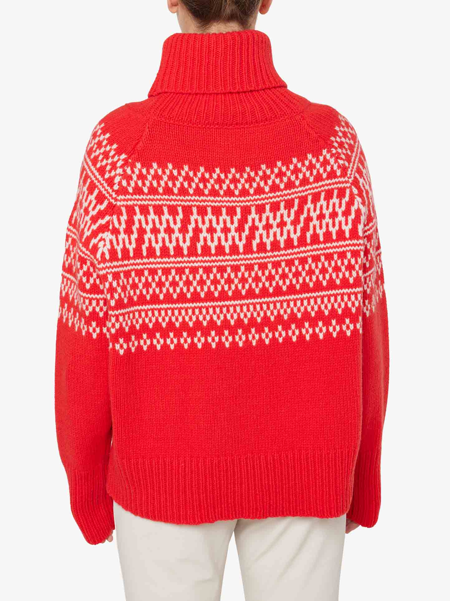 A person wearing the We Norwegians' Setesdal Sweater Women, characterized by its bright red thick-knit fabric and a white, intricate pattern on the upper half. The design is reminiscent of traditional Norwegian knits with various geometric shapes and symmetrical details. Featuring a turtleneck, this cozy sweater is photographed from behind.