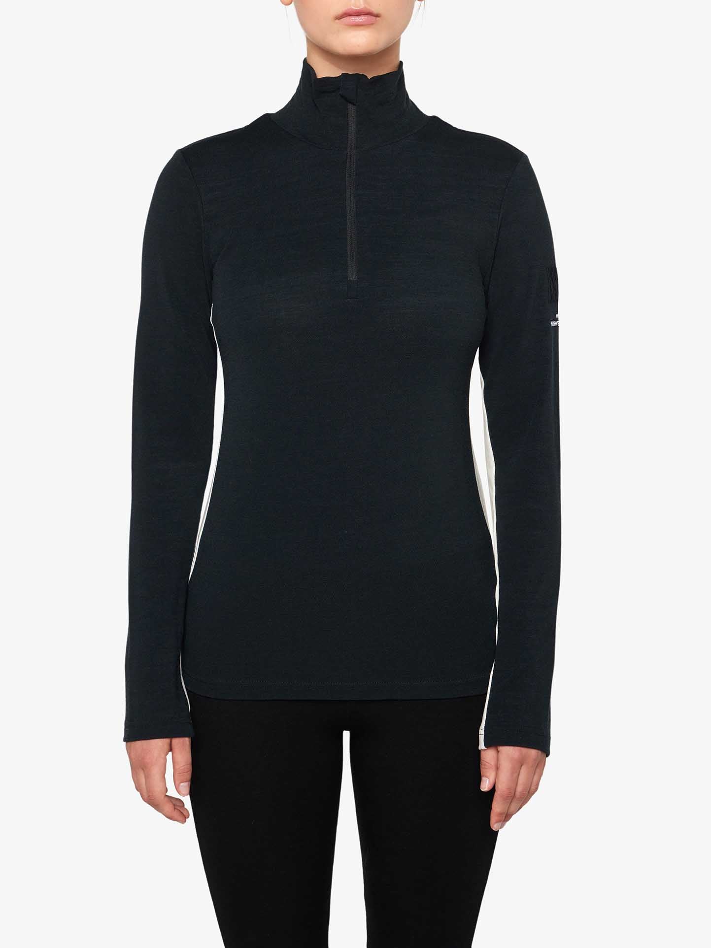 A person wearing a black Voss 1/4-Zip Women pullover by We Norwegians and black pants stands against a white background. The pullover, featuring subtle seam detail and color block panels, has a high collar. The person's hands are relaxed by their sides.