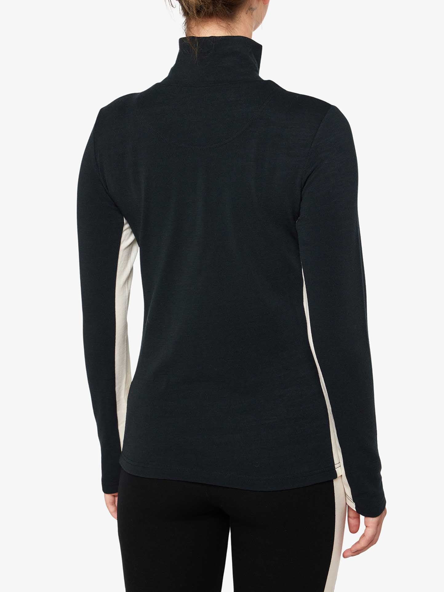 A person with hair tied back is shown from the back wearing the Voss 1/4-Zip Women top by We Norwegians. This black long-sleeve, high-neck athletic top features white color block panels. The person is also wearing black leggings, set against a plain white background.