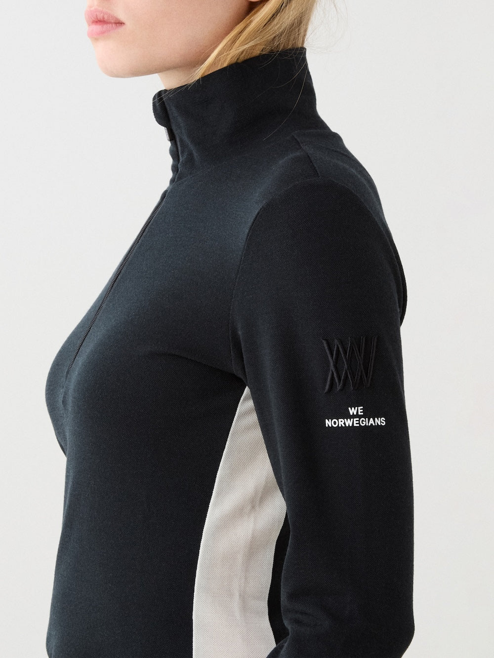 We Norwegians | FW25 | Womens Voss 1/4-Zip_Black | Model is wearing this light knit top with a stand collar, 1/4th zipper opening and long sleeves - paired with black pants on an off-white background | Close-up