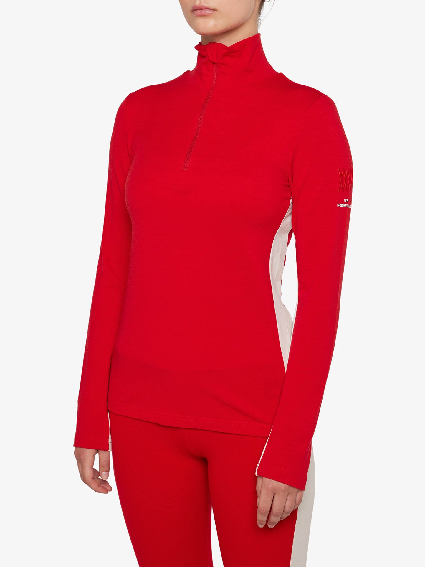 A person wearing a red Voss 1/4-Zip Women top from We Norwegians paired with matching red pants. The top features white color block panels and a small We Norwegians brand logo on the left sleeve. The background is plain white.