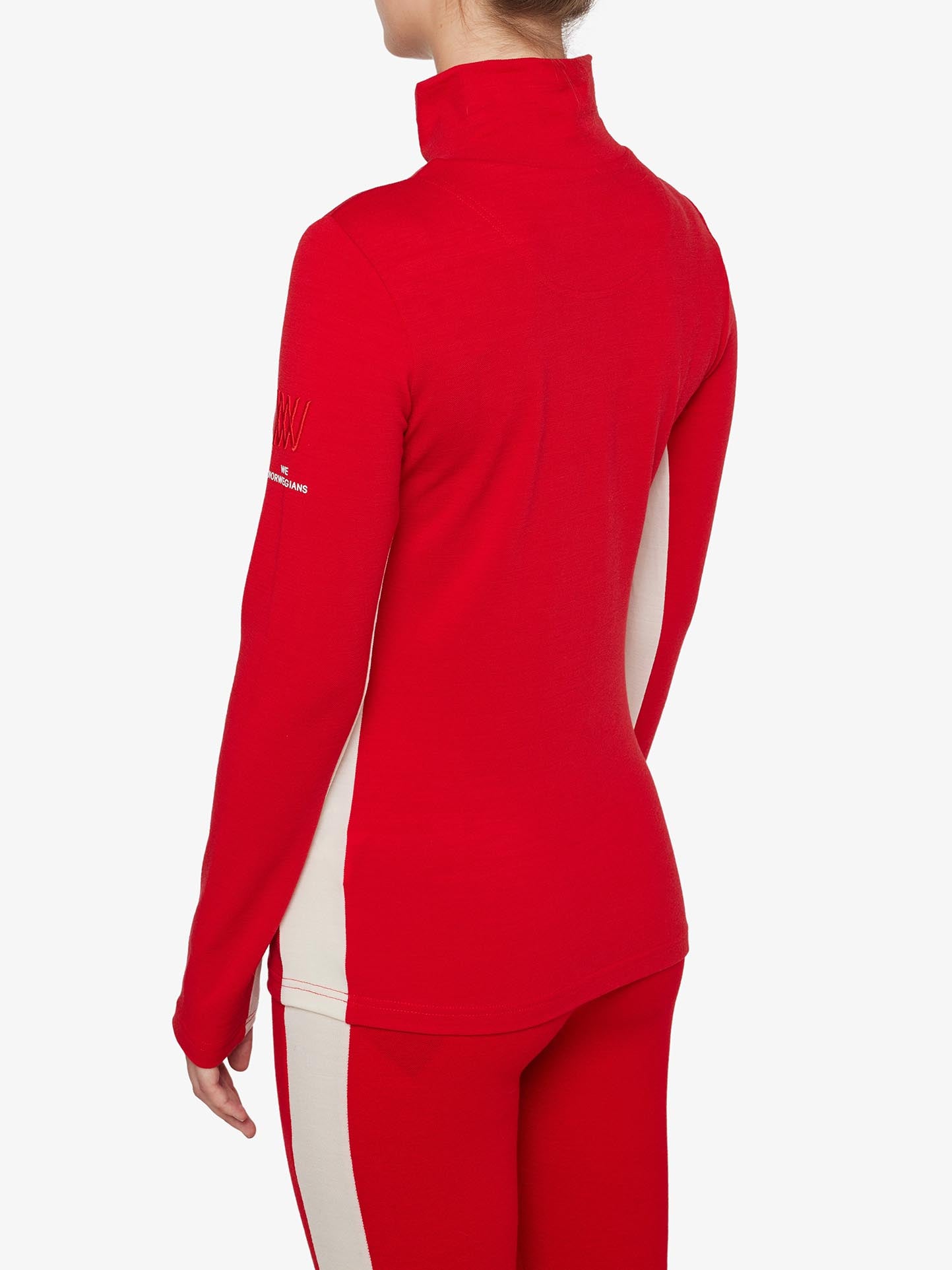 A person stands facing away, wearing a red, long-sleeve Voss 1/4-Zip Women athletic jacket by We Norwegians, featuring color block panels and matching red pants. The jacket has white side panels and a design on the left sleeve. The background is plain white.