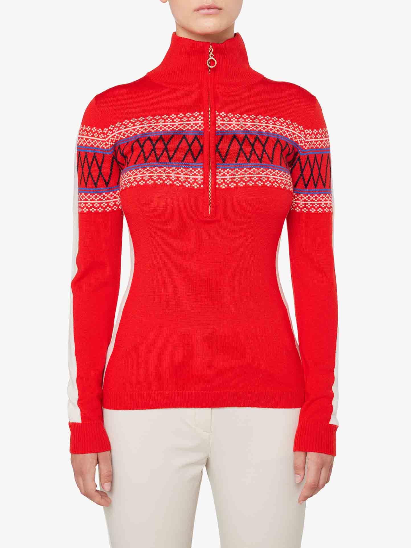 A person is wearing the Signature 1/4-Zip Women by We Norwegians, a fitted, long-sleeve red sweater crafted from fine Merino wool. It features a high collar and an intricate Setesdal pattern with white and black designs across the chest and upper arms. The person is also wearing white pants against a plain white background.