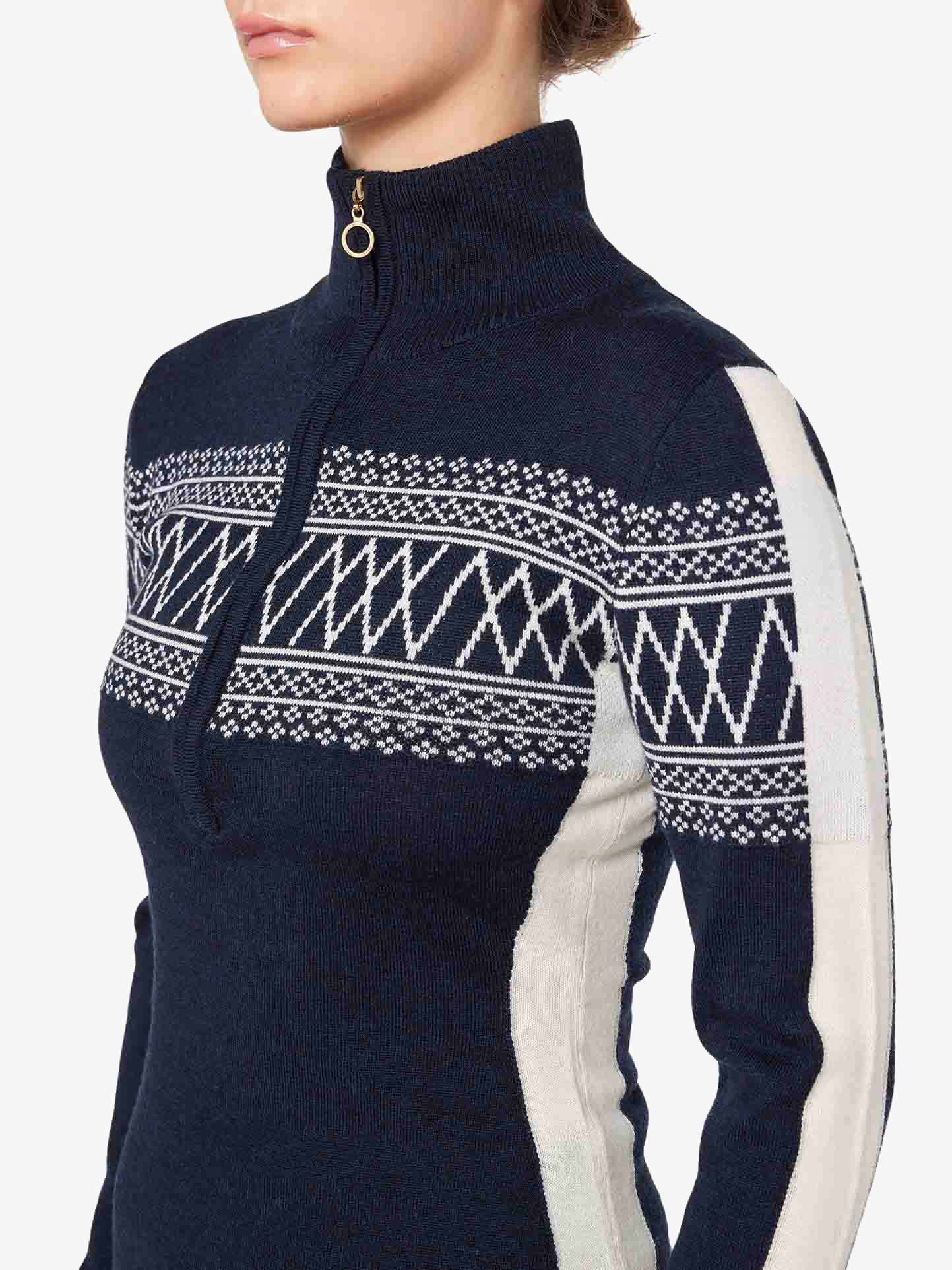 A person is wearing a navy blue "Signature 1/4-Zip Women" sweater by We Norwegians, featuring a high collar and a gold zipper. The sweater showcases white and navy Setesdal patterns across the chest and down the sleeves, along with white side panels along the torso. The person's face is not visible.