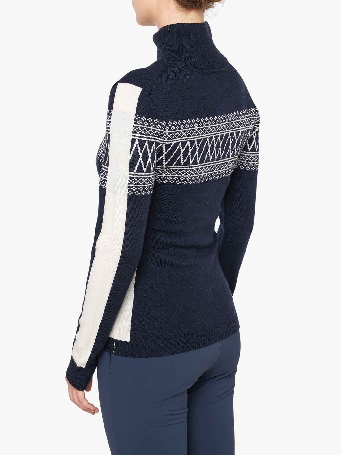 A person is wearing the We Norwegians Signature 1/4-Zip Women sweater, which is dark blue and made of fine Merino wool. It features white geometric Setesdal patterns across the upper back and sleeves, with a wide vertical white stripe on the right arm. The person is facing away, showing the back and side profile of the sweater.