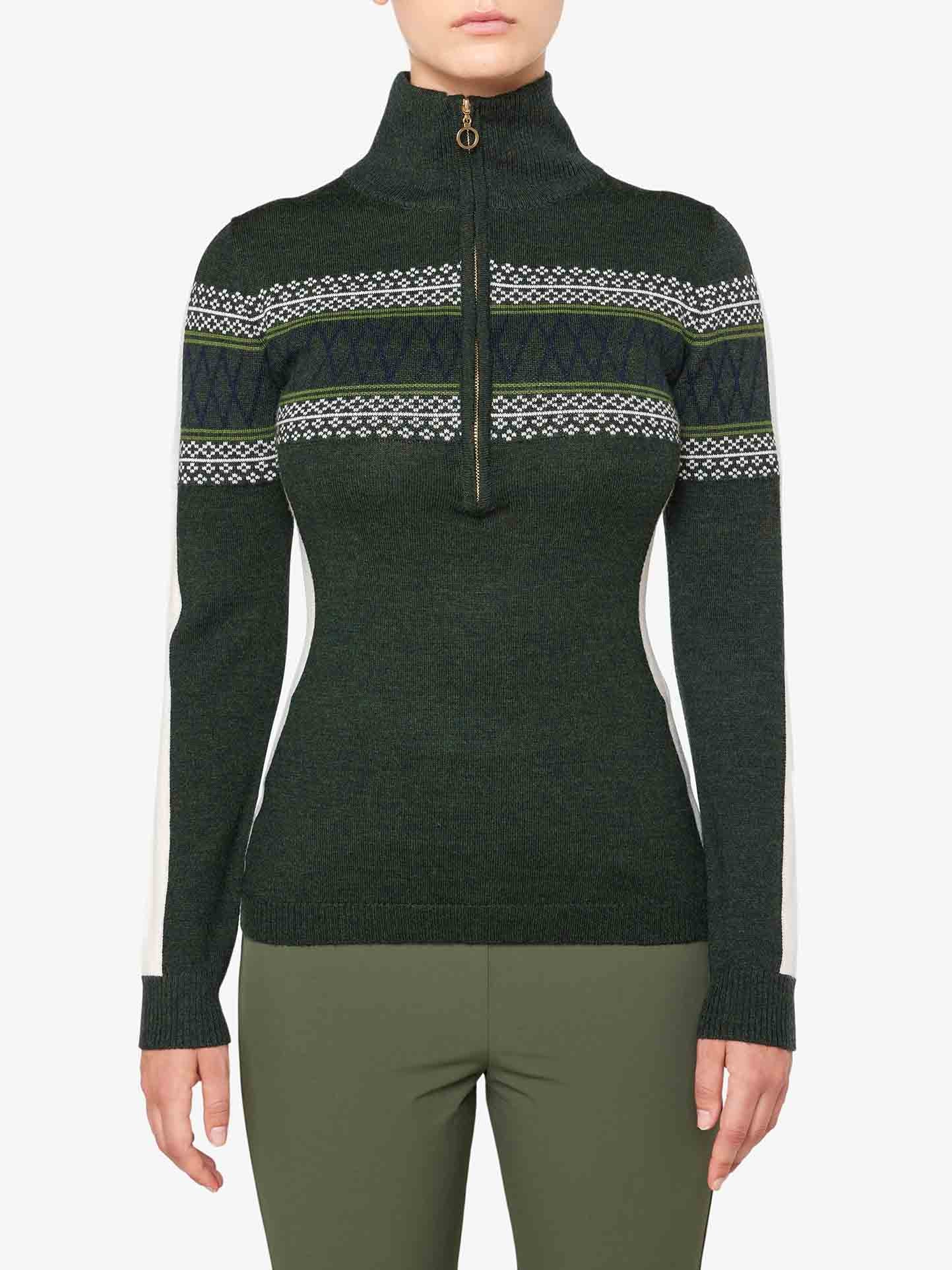 Someone is wearing the Signature 1/4-Zip Women by We Norwegians, an olive green sweater featuring intricate white and dark green Setesdal patterns across the chest and sleeves. The sweater, made from fine Merino wool, boasts a slim fit design and white side panels. The outfit is completed with light green pants.