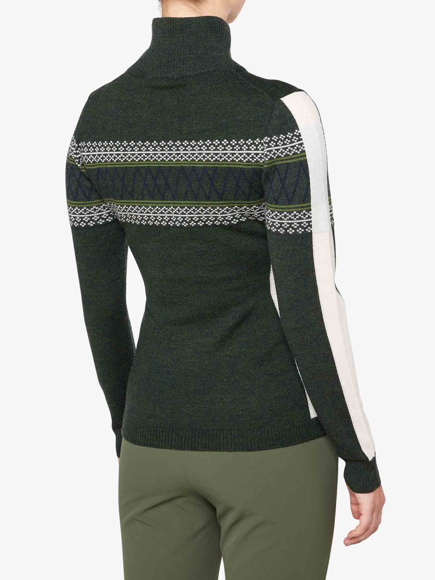 A person is wearing the Signature 1/4-Zip Women by We Norwegians, a dark green turtleneck sweater featuring a white and dark green Setesdal pattern stripe across the chest and arms. This fine Merino wool sweater also has white panels on the sides of the arms. The person is also wearing green pants, and their back is shown.