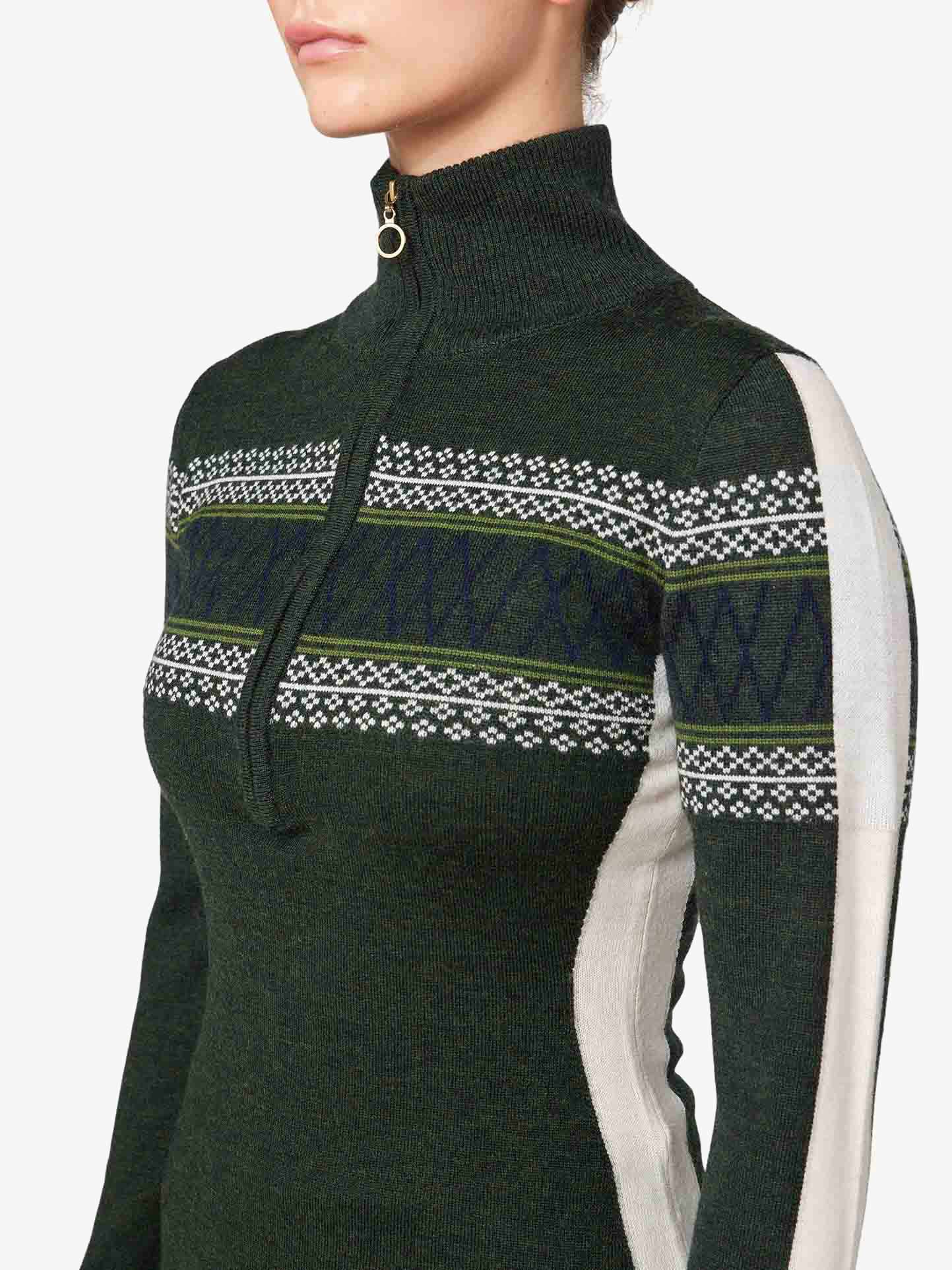 A close-up view shows a person wearing the We Norwegians Signature 1/4-Zip Women sweater in dark green. This fine Merino wool sweater is adorned with a Setesdal pattern band in lighter shades, including white and green, across the chest and shoulders. Additionally, it features light-colored panels along the sleeves.