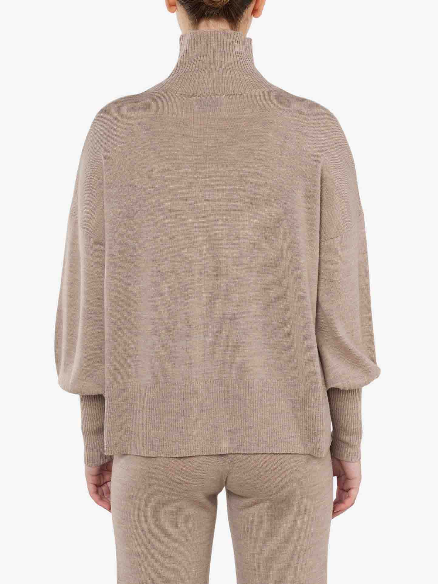 A person is shown from the back wearing the Geilo Oversized Sweater Women by We Norwegians and matching pants. The merino wool sweater features a funnel neck collar and long sleeves, exuding a cozy yet refined look. The background is plain white.