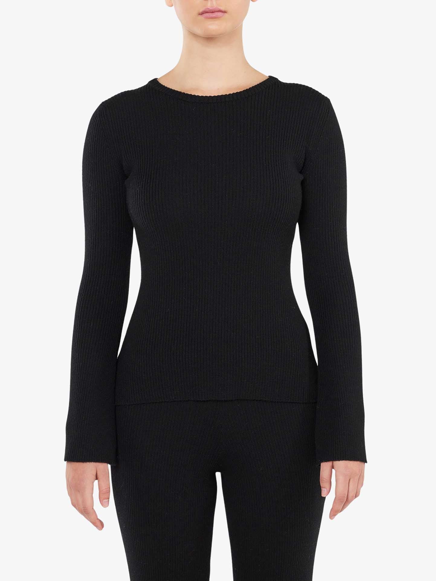 A person wearing the We Norwegians Geilo Ribbed Sweater for women is shown from mid-thigh up. The fitted, black, long-sleeve sweater features a simple round neckline. The background is plain white.