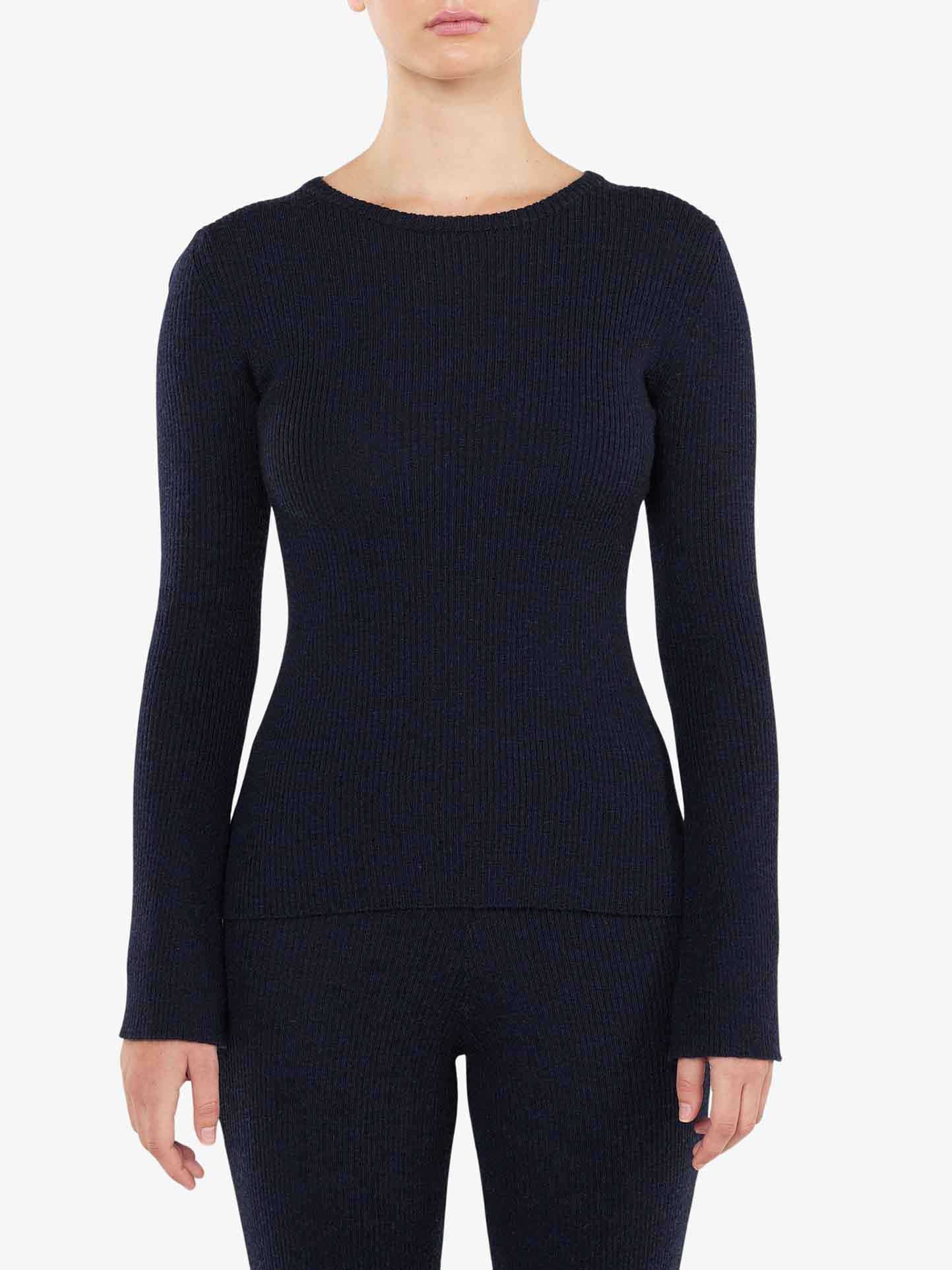 A person in a form-fitting, long-sleeve, dark navy blue Geilo Ribbed Sweater Women by We Norwegians. The individual is wearing matching navy blue knit pants. The background is plain white, highlighting the outfit made of merino wool. The person's face is not visible in the image.