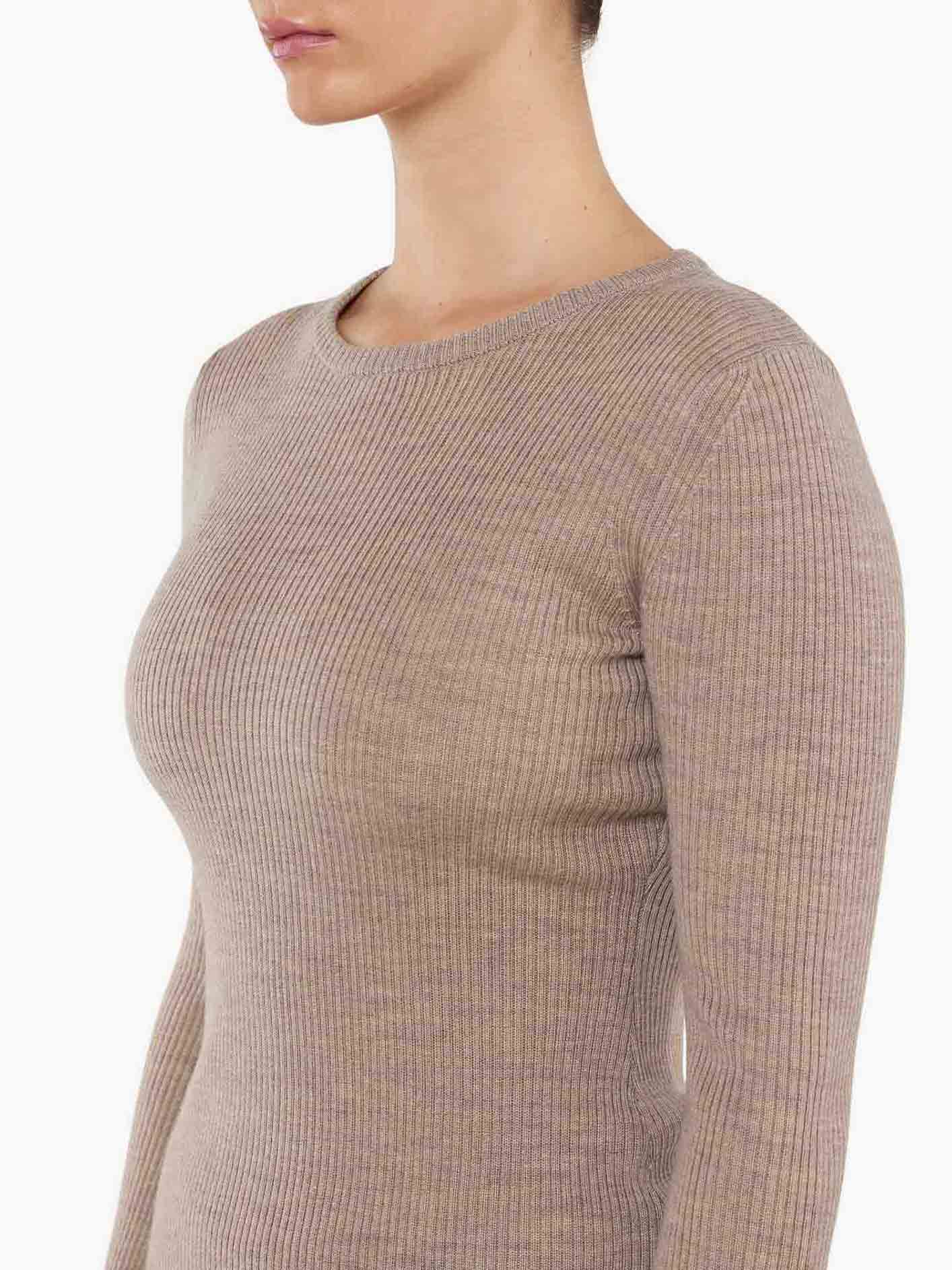 Side profile of a person wearing the We Norwegians Geilo Ribbed Sweater Women, a fitted, ribbed, long-sleeve, beige knit top. The image focuses on the torso and part of the face without revealing the identity. The fabric's texture and close-fitting style are clearly visible, highlighting the elegance of this merino wool piece.