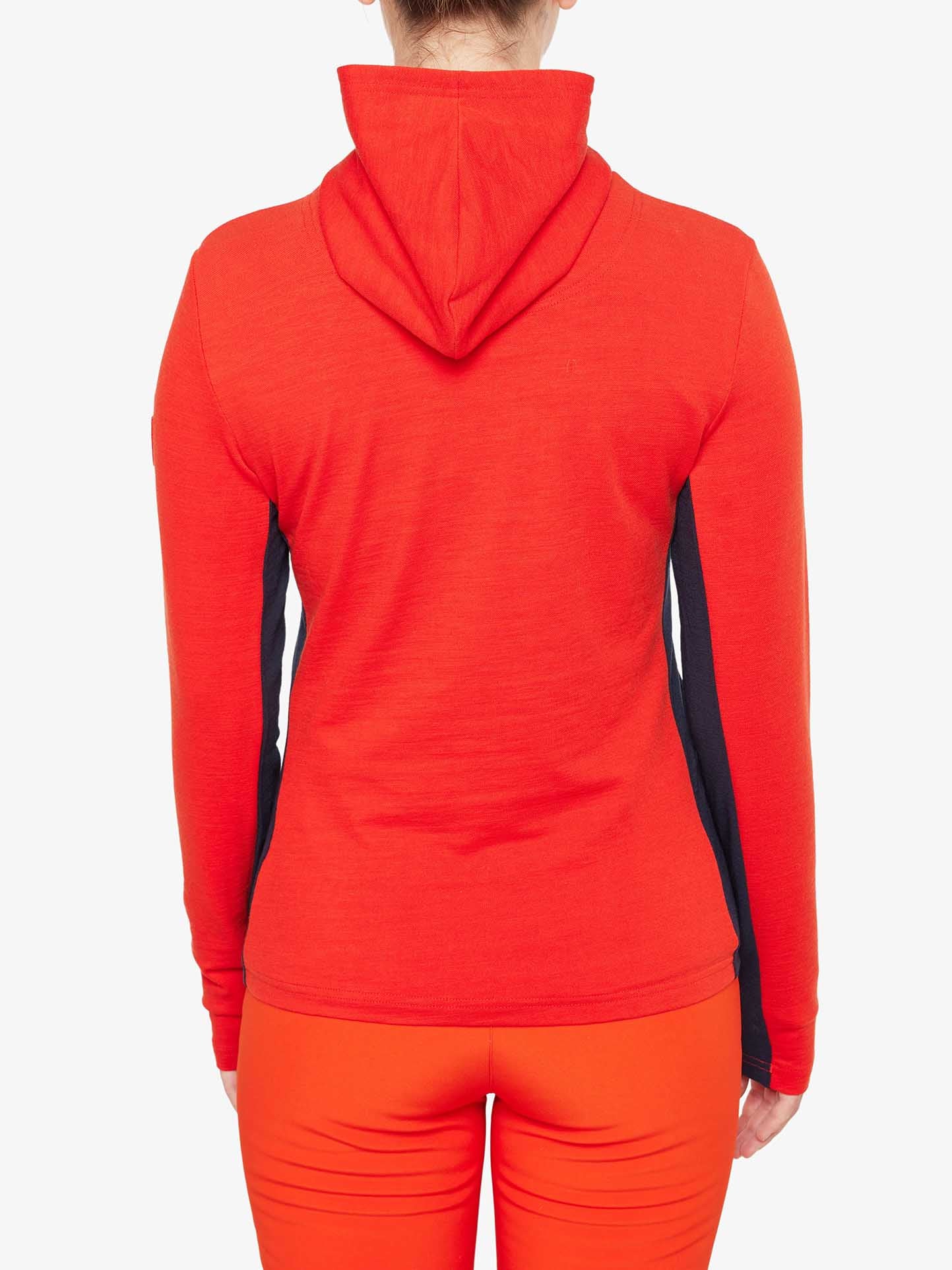 A person is facing away from the camera, wearing a bright orange Ski Fullzip Hoodie Women by We Norwegians and matching orange pants. The hoodie features retro color block panels in black on the sides. The background is plain white.