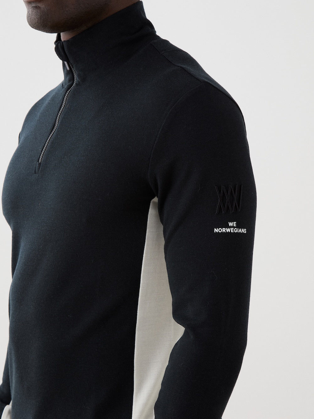 We Norwegians | FW25 | Mens Voss 1/4-Zip_Black | Model is wearing this light weight knitted top with a stand collare, 1/4th zipper opening and long sleeves on an off-white background | Close-up