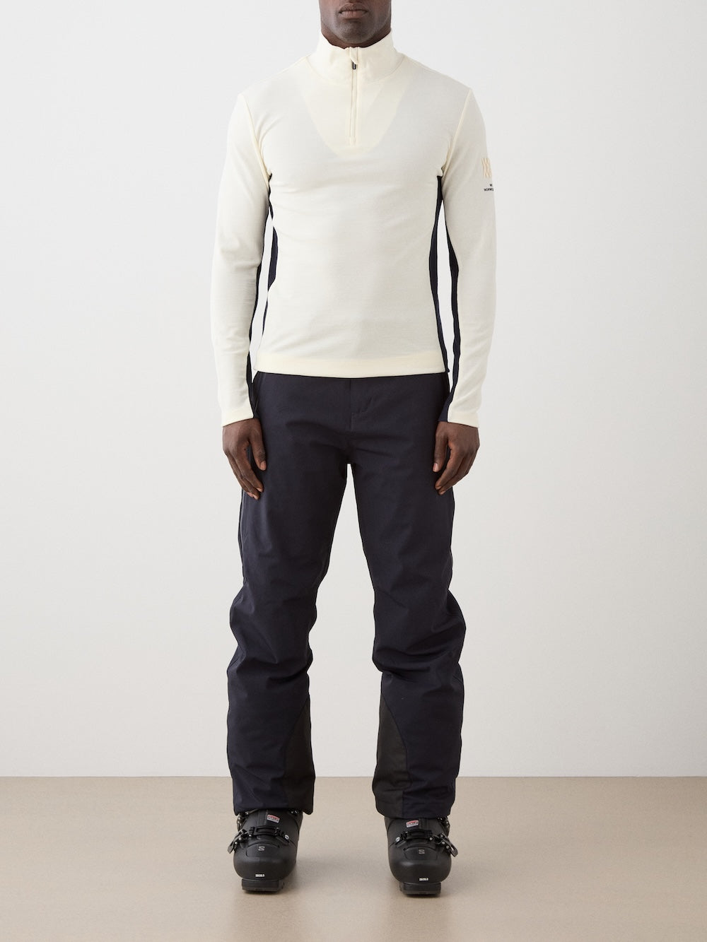 We Norwegians | FW25 | Mens Voss 1/4-Zip_Off white | Model is wearing this light weight knitted top with a stand collare, 1/4th zipper opening and long sleeves - paired with black pants on an off-white background | Front