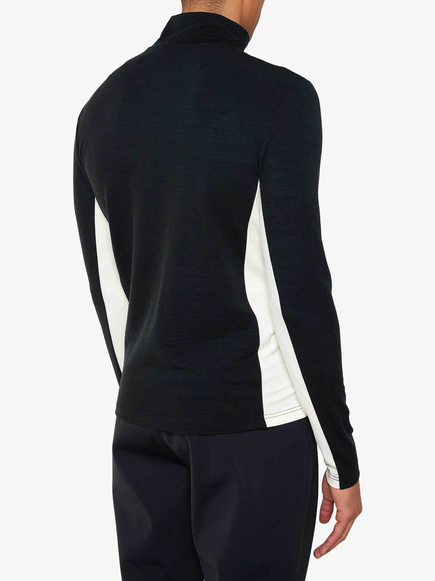 A person wearing a We Norwegians Voss 1/4-Zip Men black long-sleeve shirt with white color block panels and black pants is shown from the back. The shirt, made of Superfine Merino wool, features a high collar, and the individual stands against a plain white background.