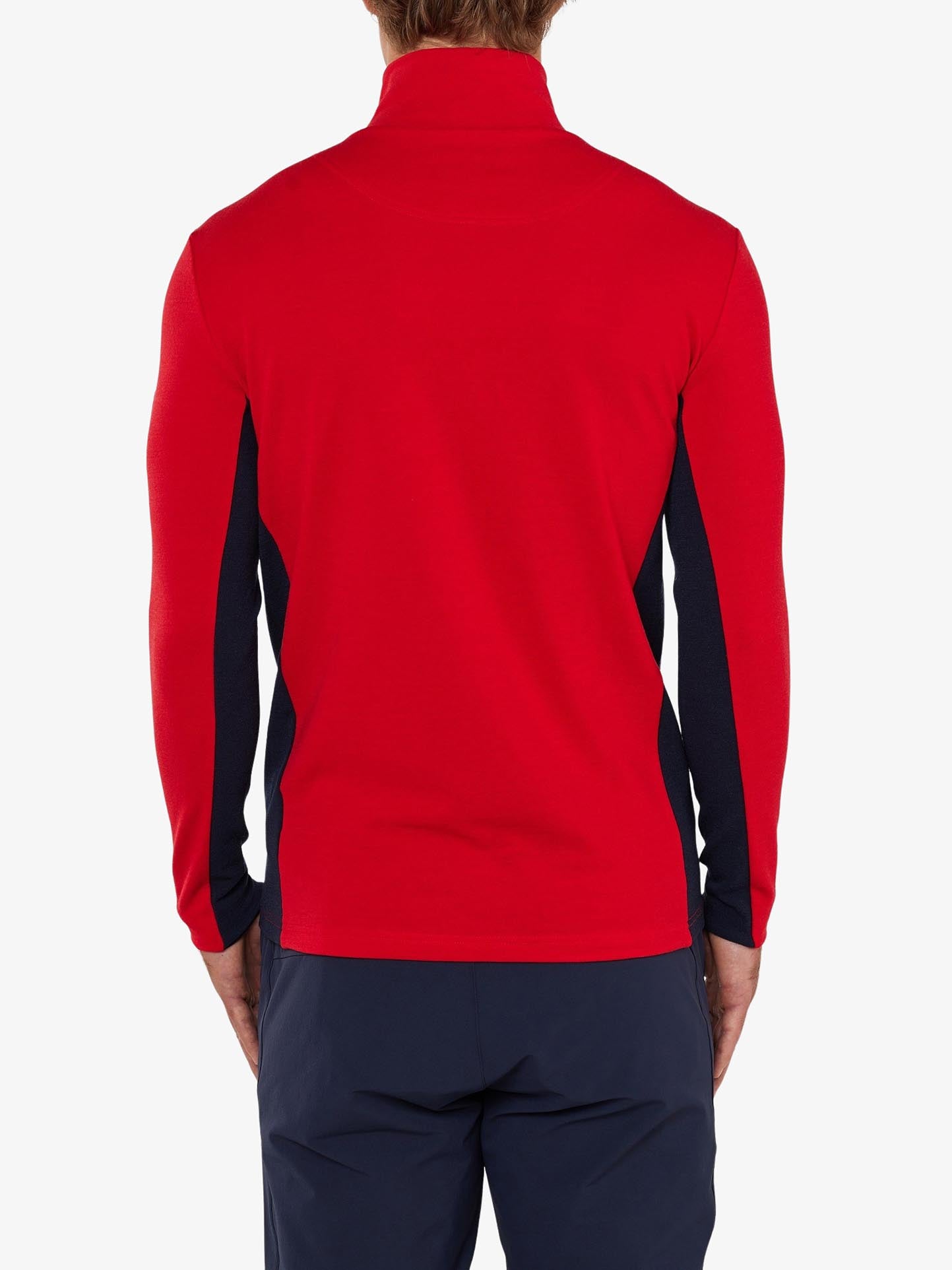 A person is turned away from the camera, wearing a red long-sleeve Voss 1/4-Zip Men by We Norwegians with black color block panels and dark blue pants. Crafted from superfine Merino wool, the shirt features a high collar. The person's arms rest by their sides against a plain white background.