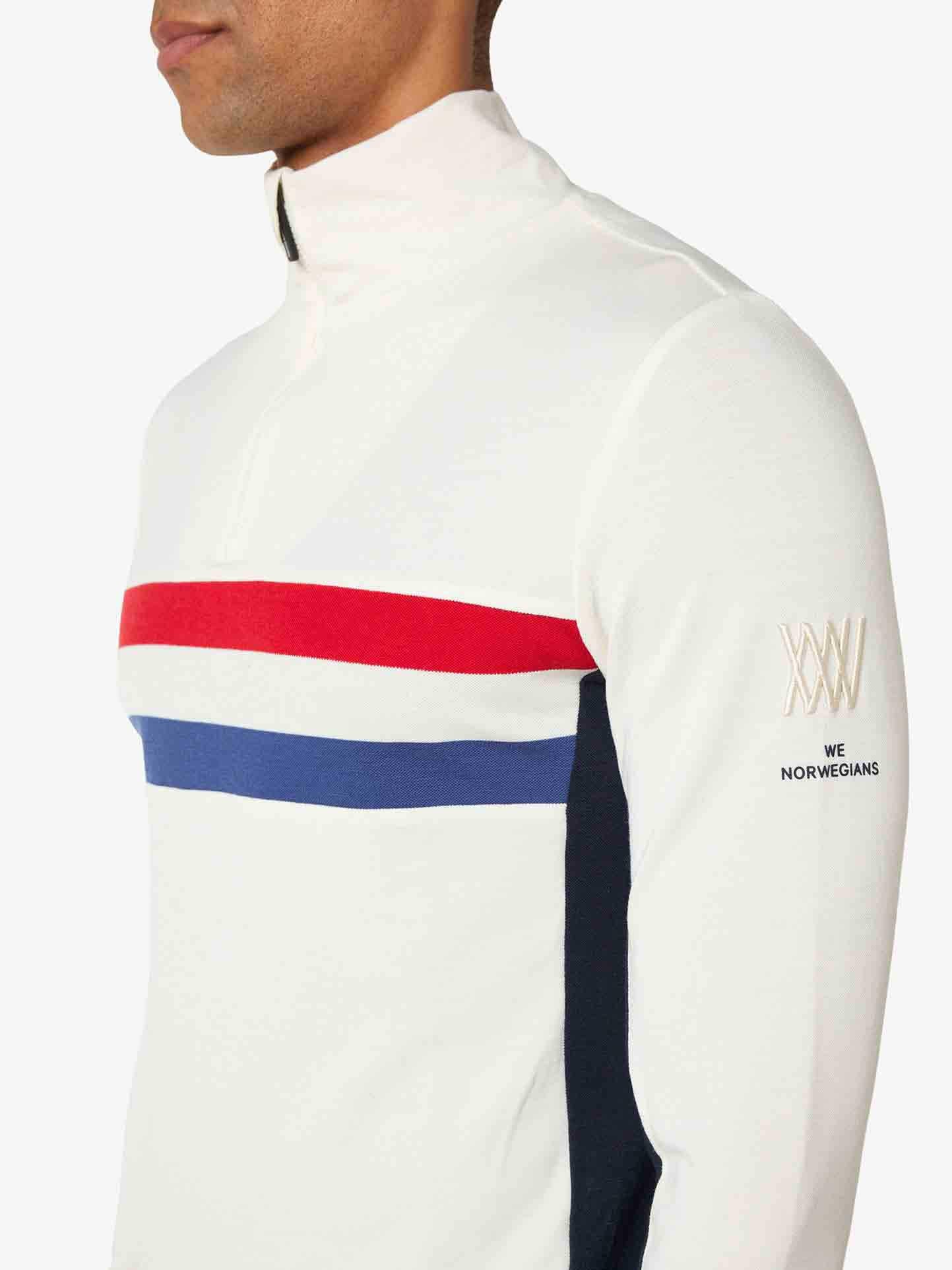 Close-up of a person wearing the Ski 1/4-Zip Men by We Norwegians. This retro-inspired base layer features horizontal red and blue stripes across the chest and "WXW" and "WE NORWEGIANS" branding on the sleeve. The background is plain white.