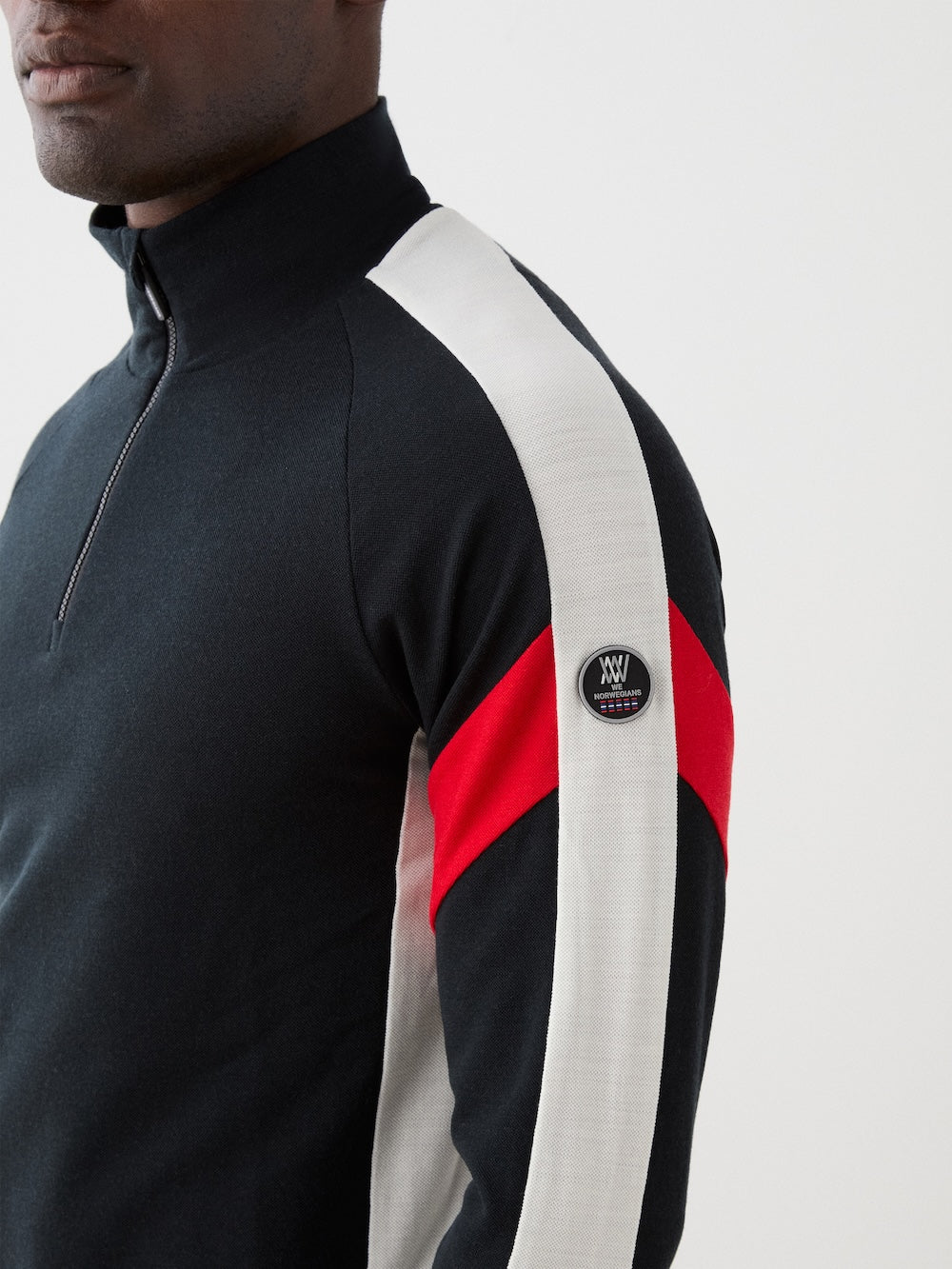 The We Norwegians Zermatt Zipup Men is a Merino wool ski sweater with a half-zip collar, black body, cream sleeves with black inner arms, diagonal red stripes, and a circular patch on the left sleeve | Close-up