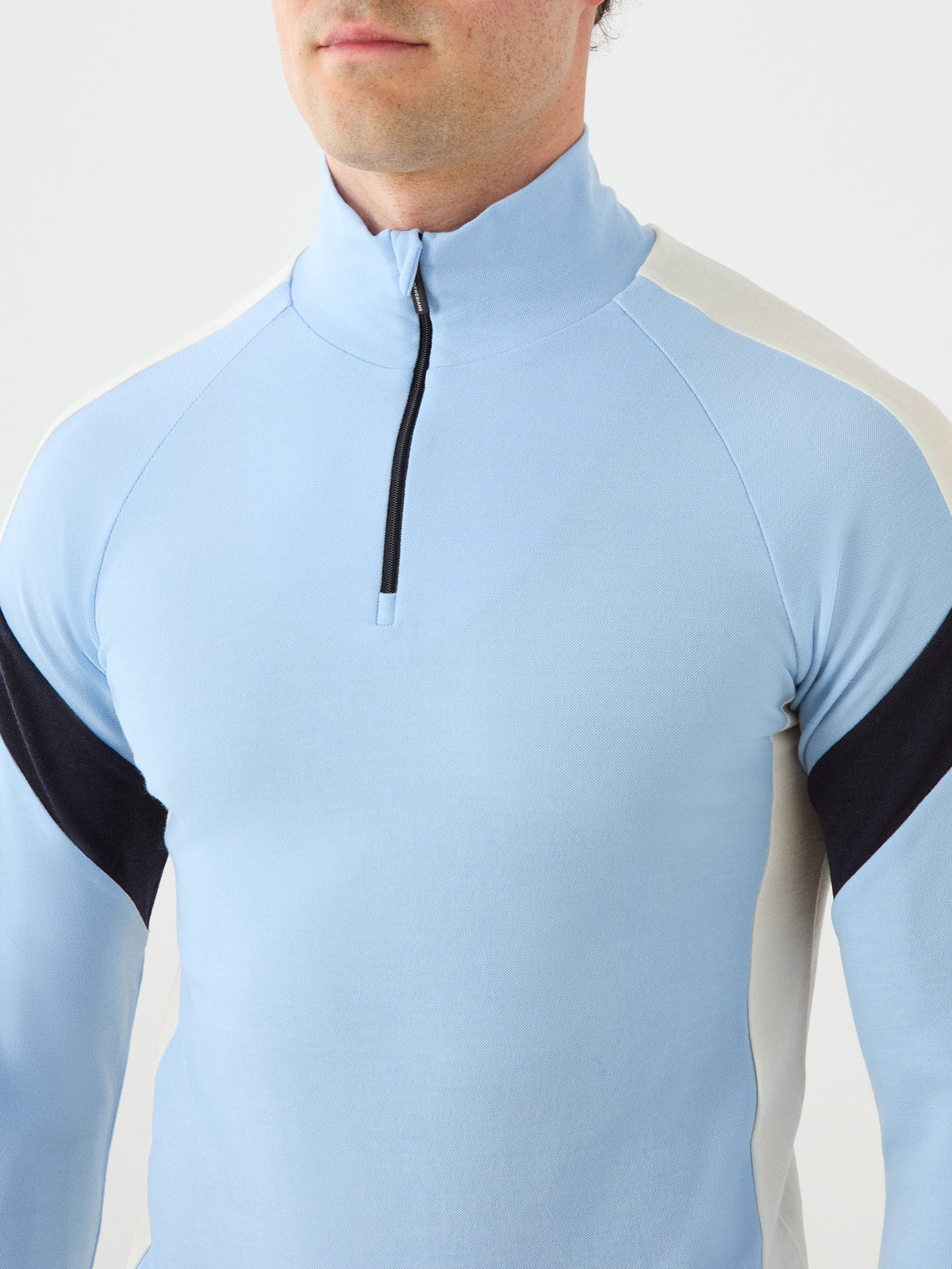 A person wearing the We Norwegians Zermatt Zipup Men in light blue—a long-sleeve, half-zip athletic top with black and white accents on the shoulders and sleeves—shown from shoulders to mid-torso.